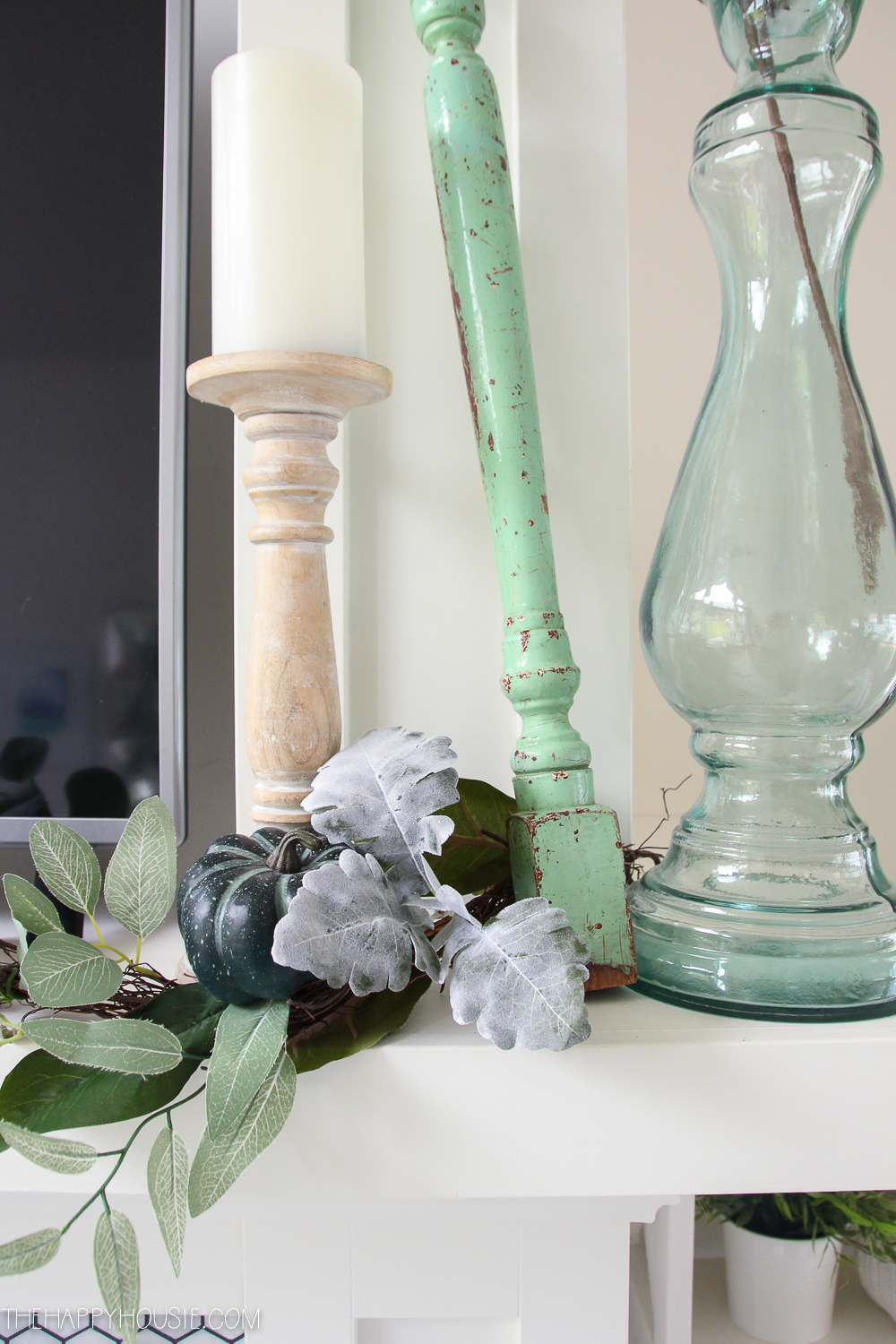 A candle, clear green glass bottle and a small pumpkin is on the mantel.