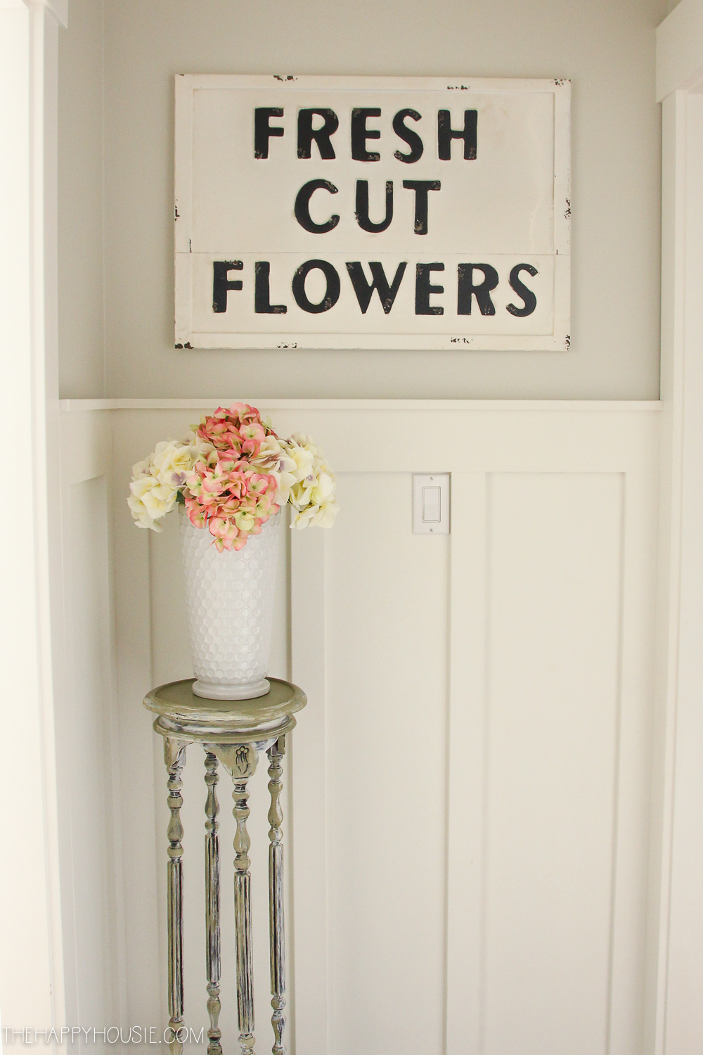A sign on the wall saying fresh cut flowers and then a vase full of flowers underneath it.