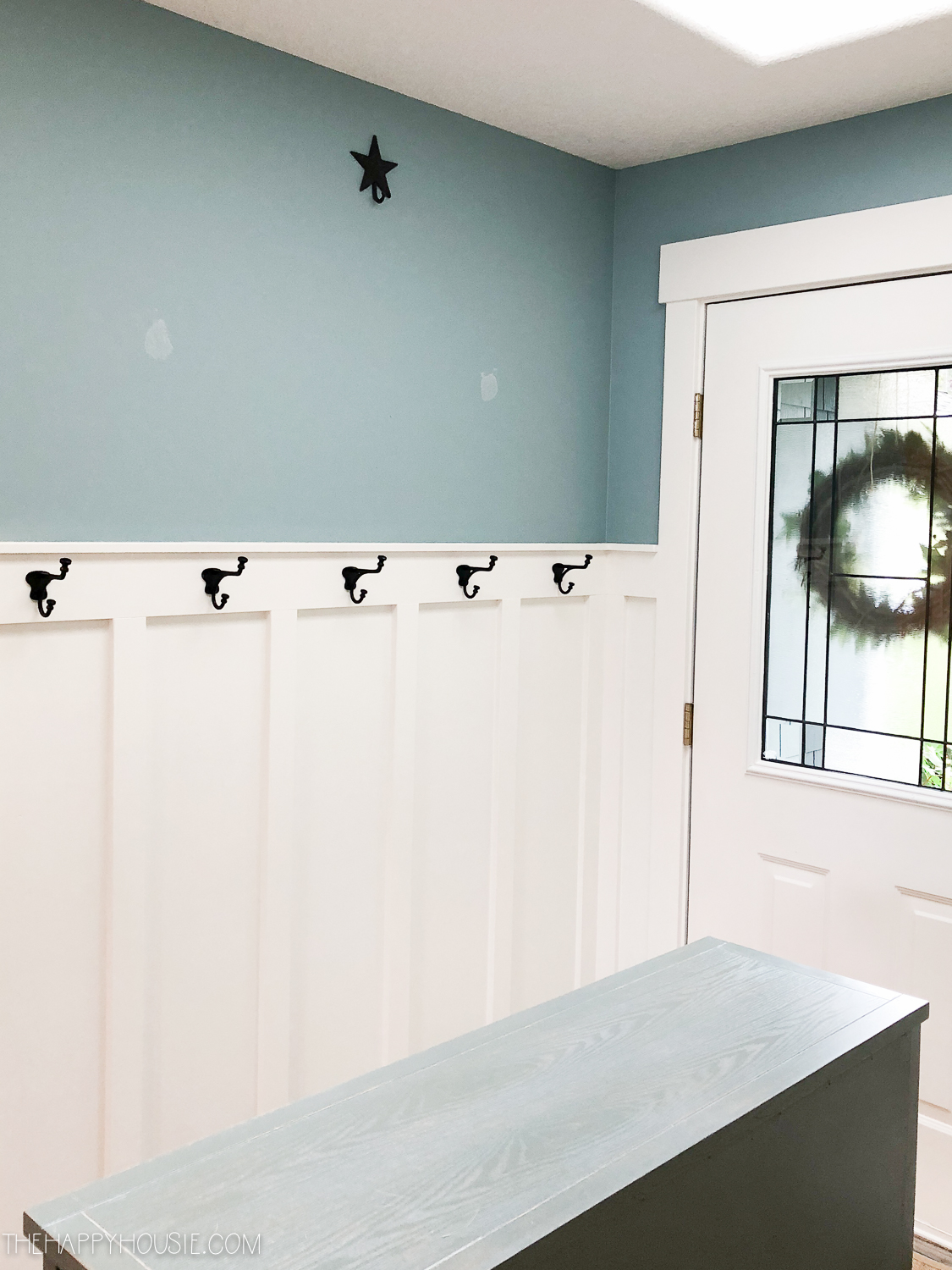 The hallway painted grey with black hooks for jackets.