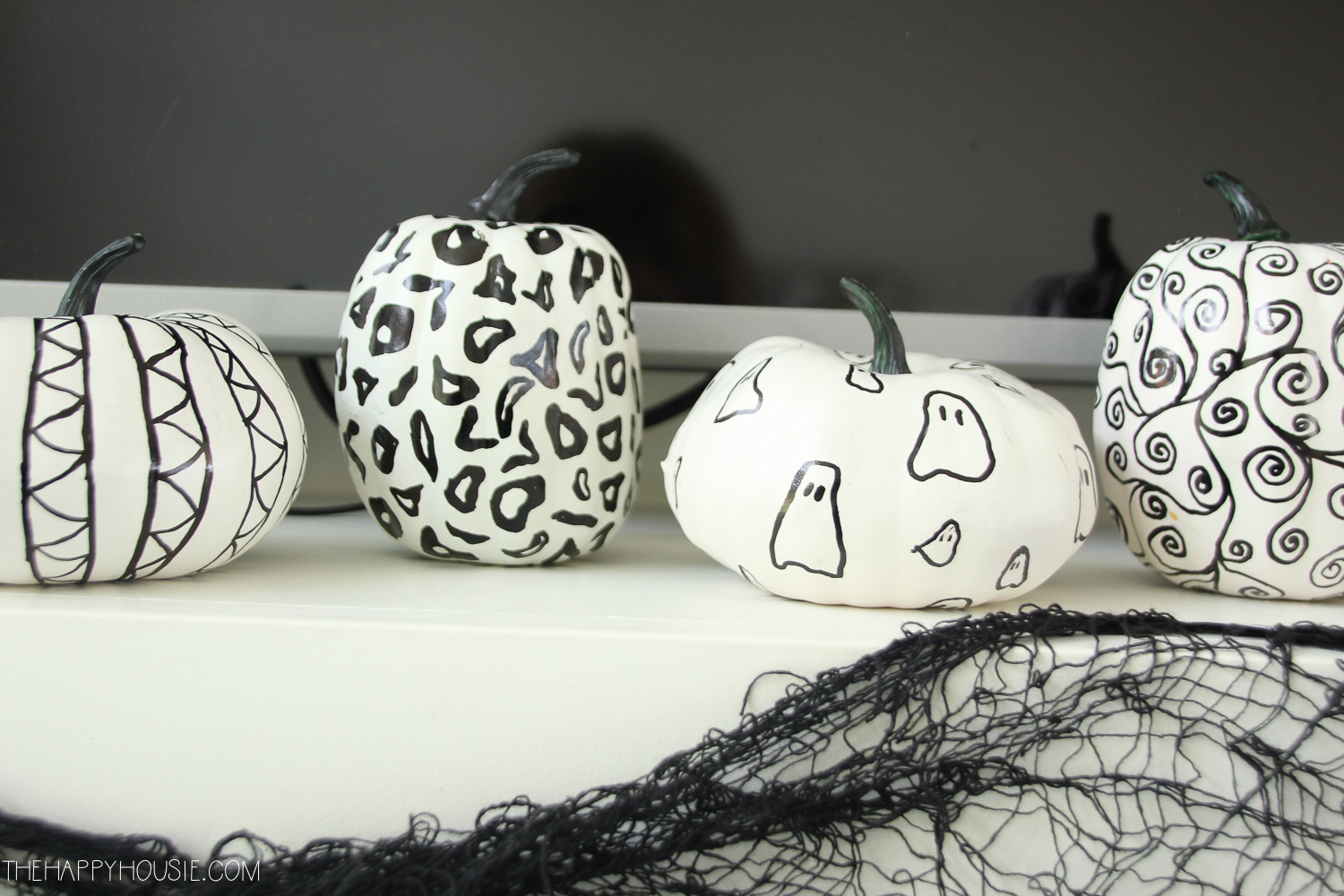 There are white pumpkins with drawings of detail on them with the black sharpie.
