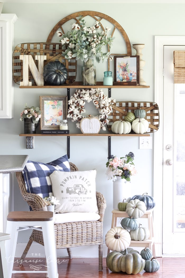 White and blue pumpkins are underneath a wooden shelf decorated for fall.
