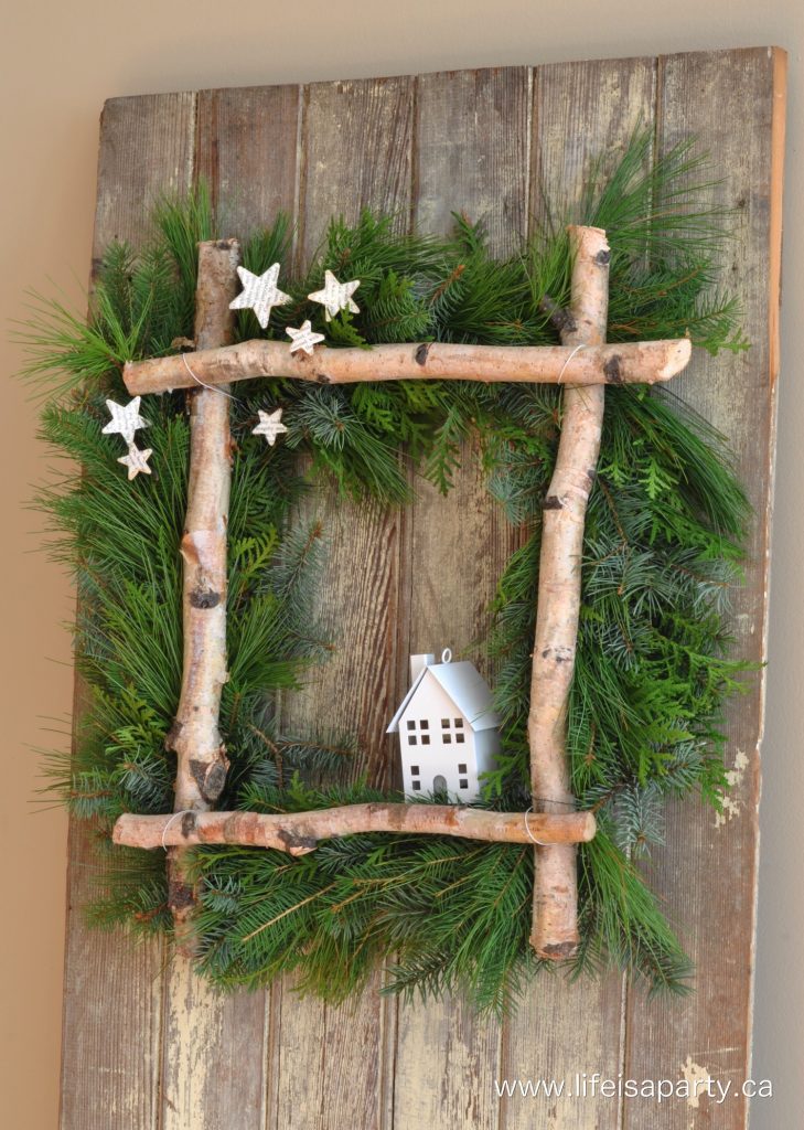 Rustic wreath with tree branches and a small wooden home on it.