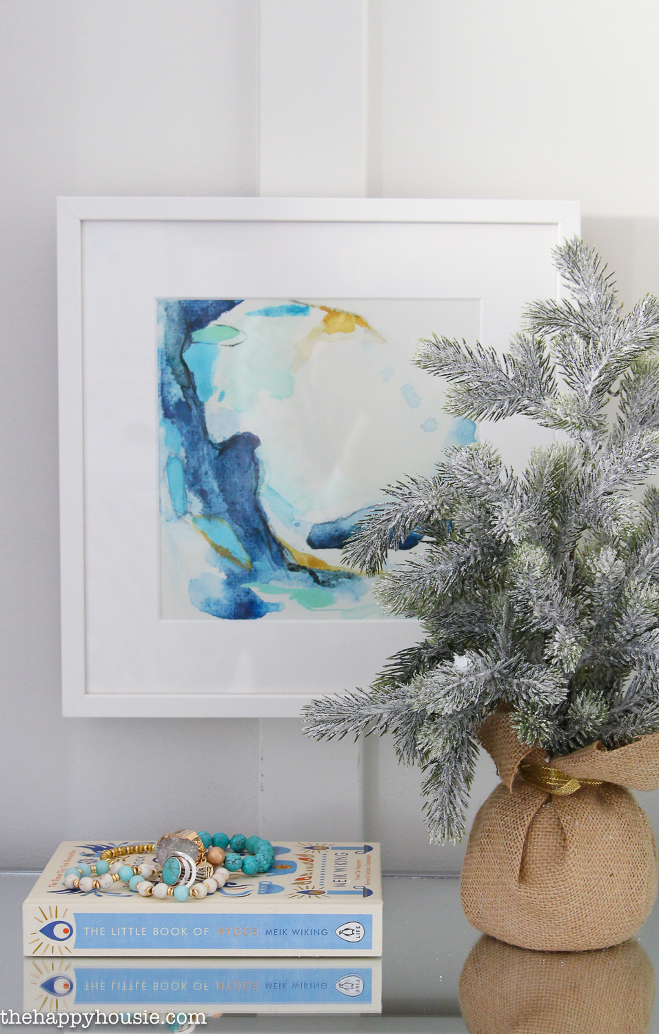A small tree on the table in front of a watercolour picture.