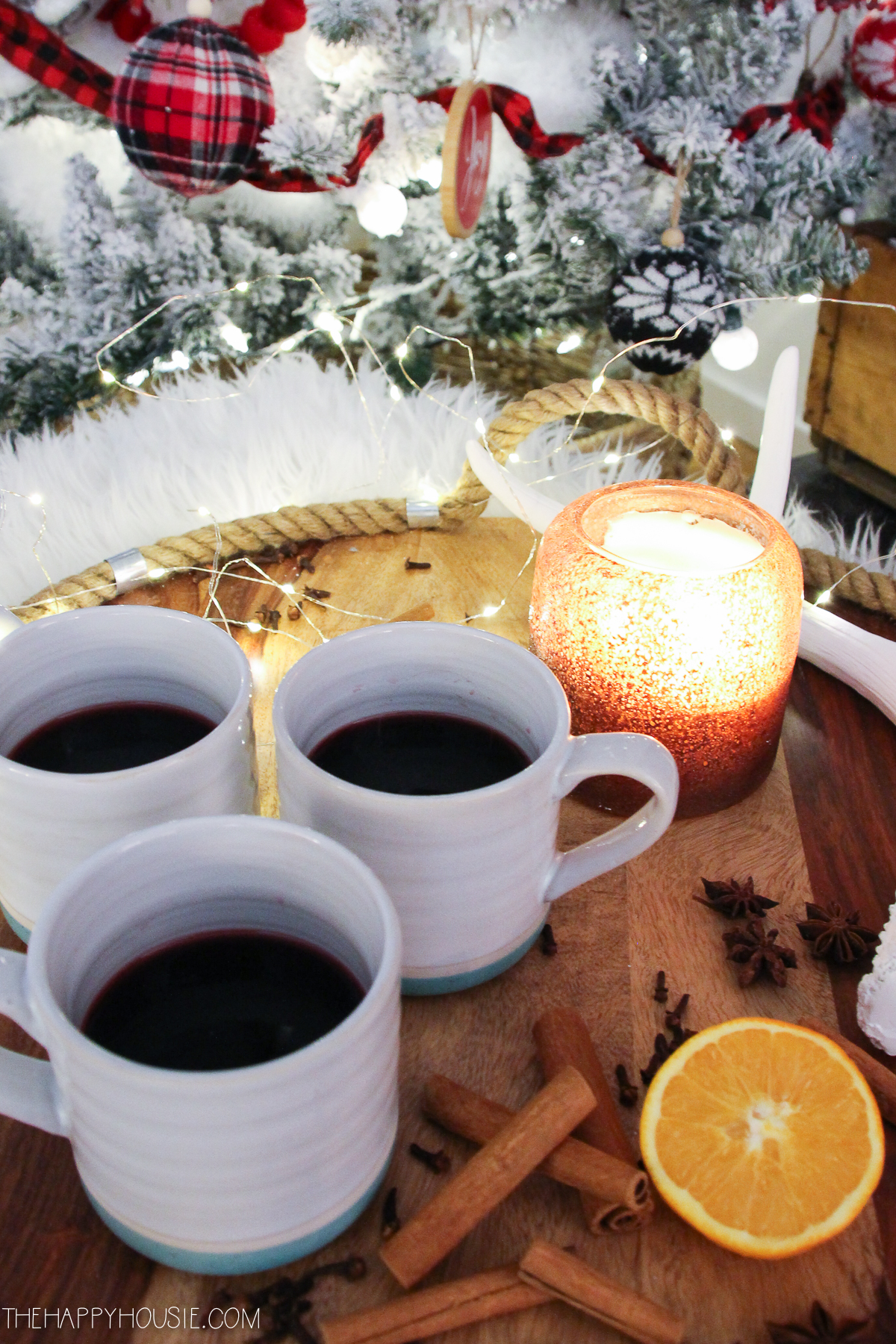 Mulled wine in mugs beside a lit candle in a votive.