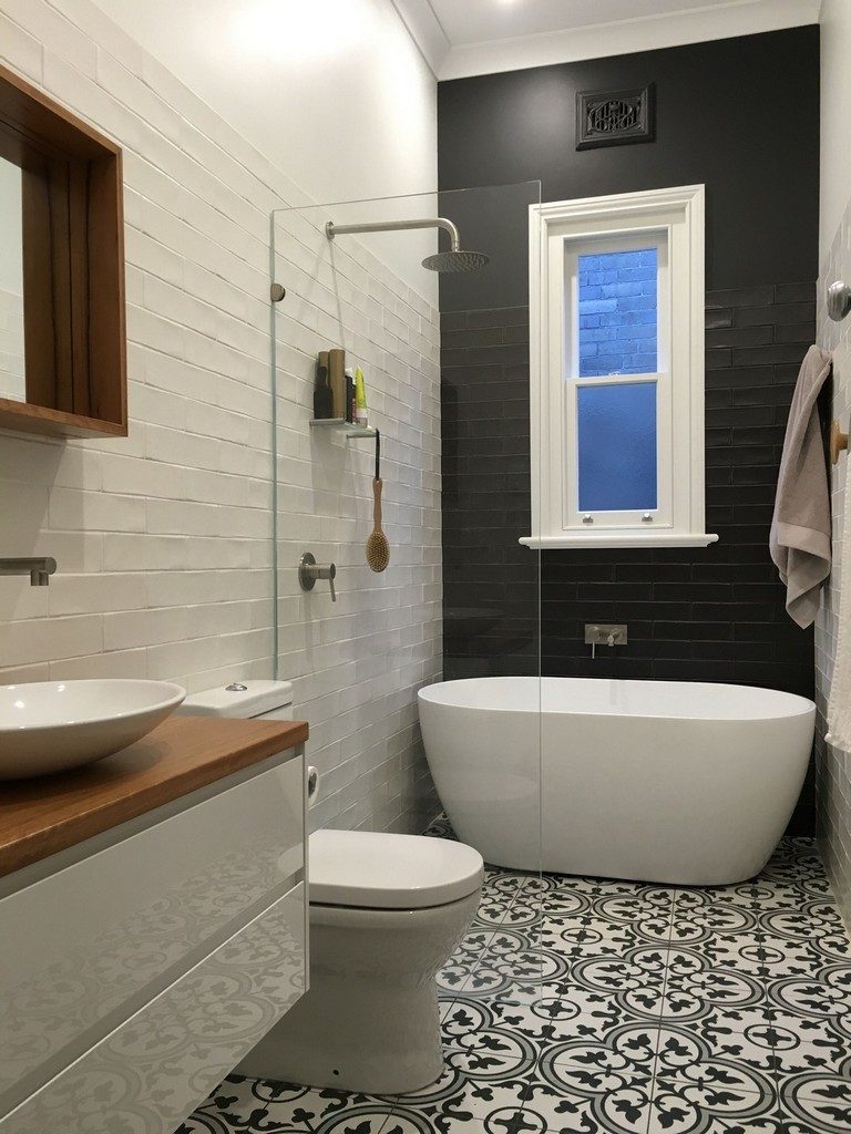 There is a free standing tub with a black wall behind it and a patterned floor.