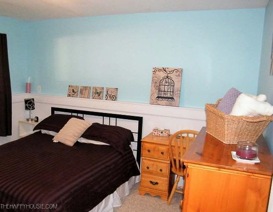 a basement guest bedroom painted blue with a bed and wooden dresser and desk
