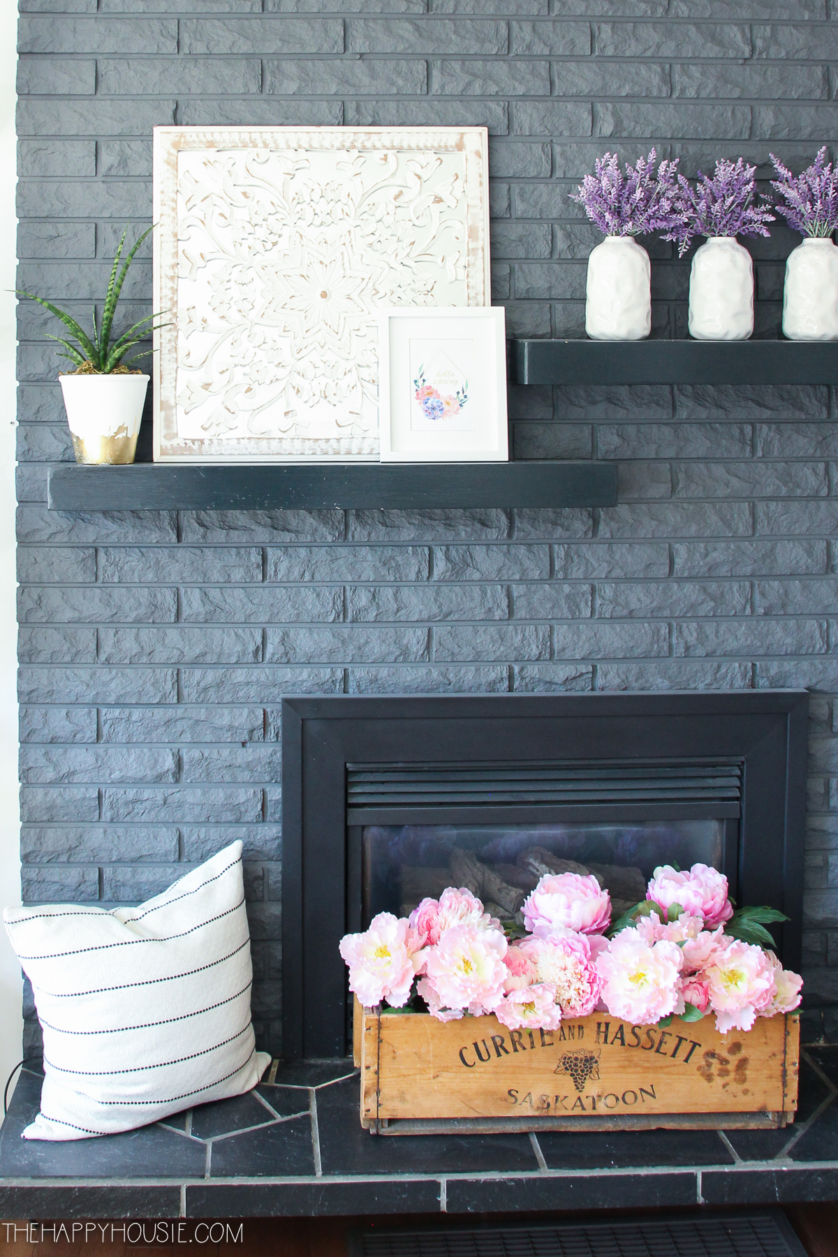 The mantel decor is vases with lilac and small pictures and a potted plant.