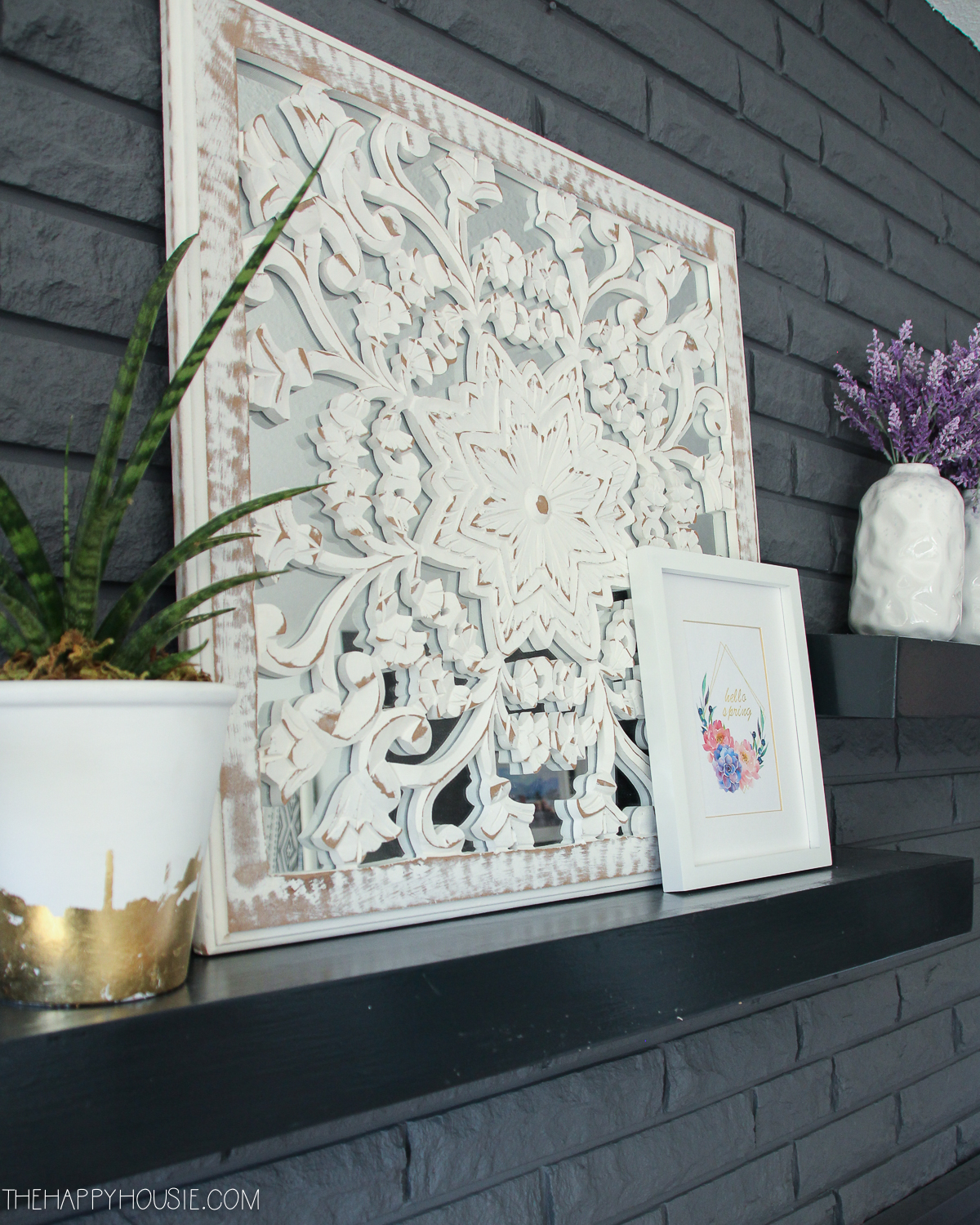 Fireplace shelves decorated with pictures, a plant and flowers in white vases.