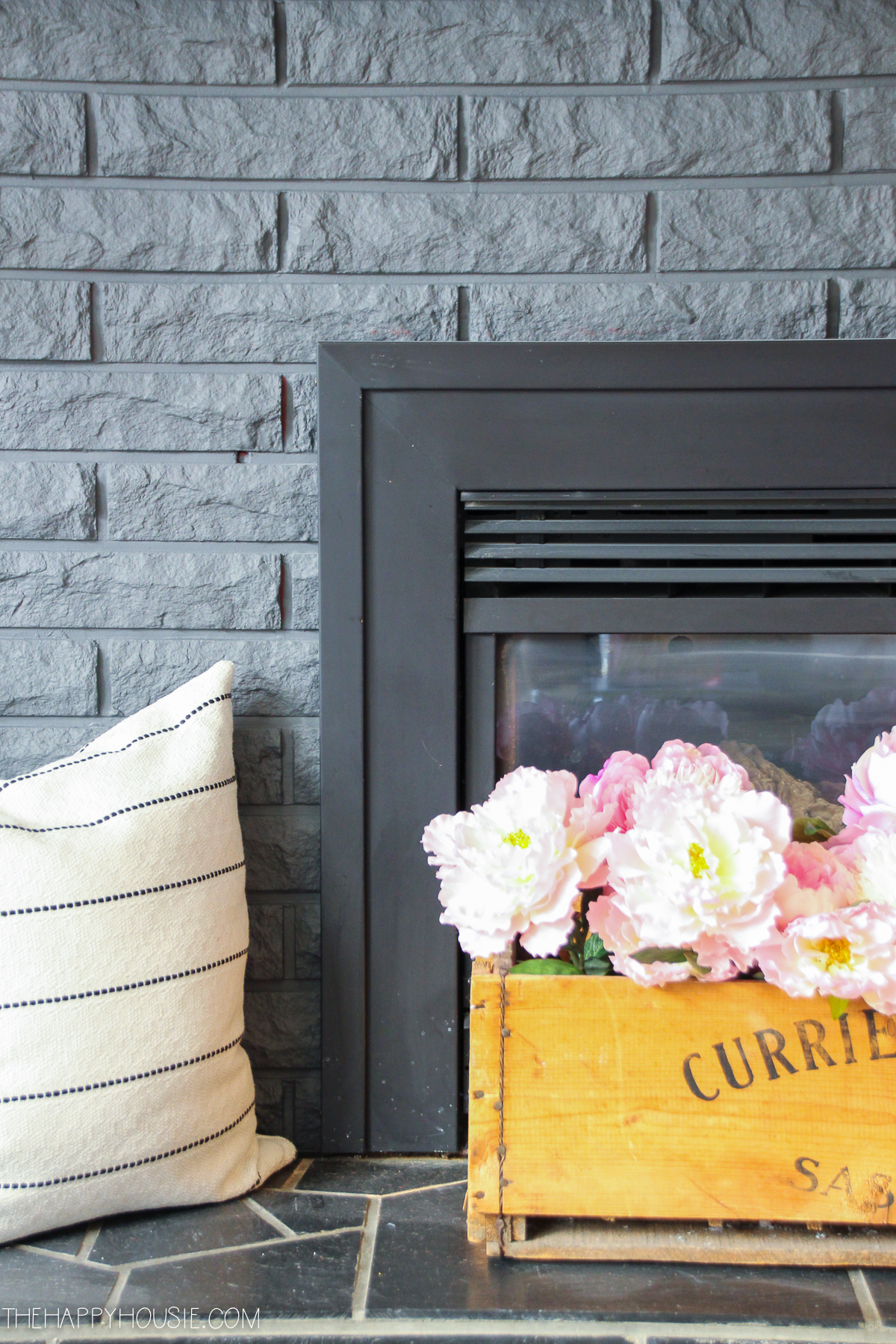 Up close picture of the fireplace with peonies in front of it in a wooden box.