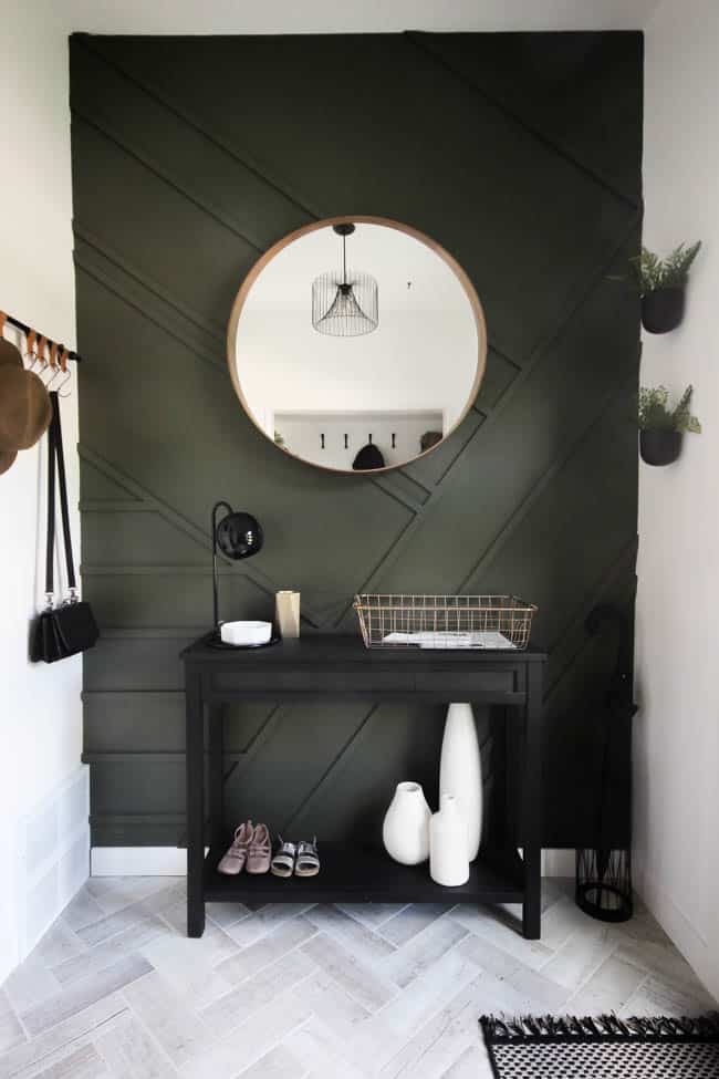 Dark olive green panelled wall with a round mirror and a small desk underneath.