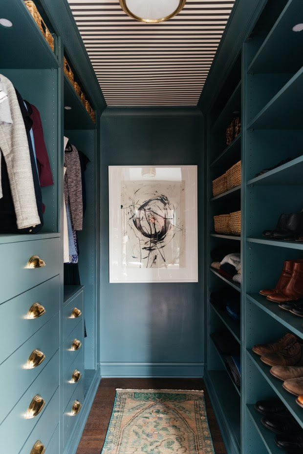 a walk-in closet painted out in dark teal green featuring an Ikea PAX system that has been hacked to give a custom built-in closet feel