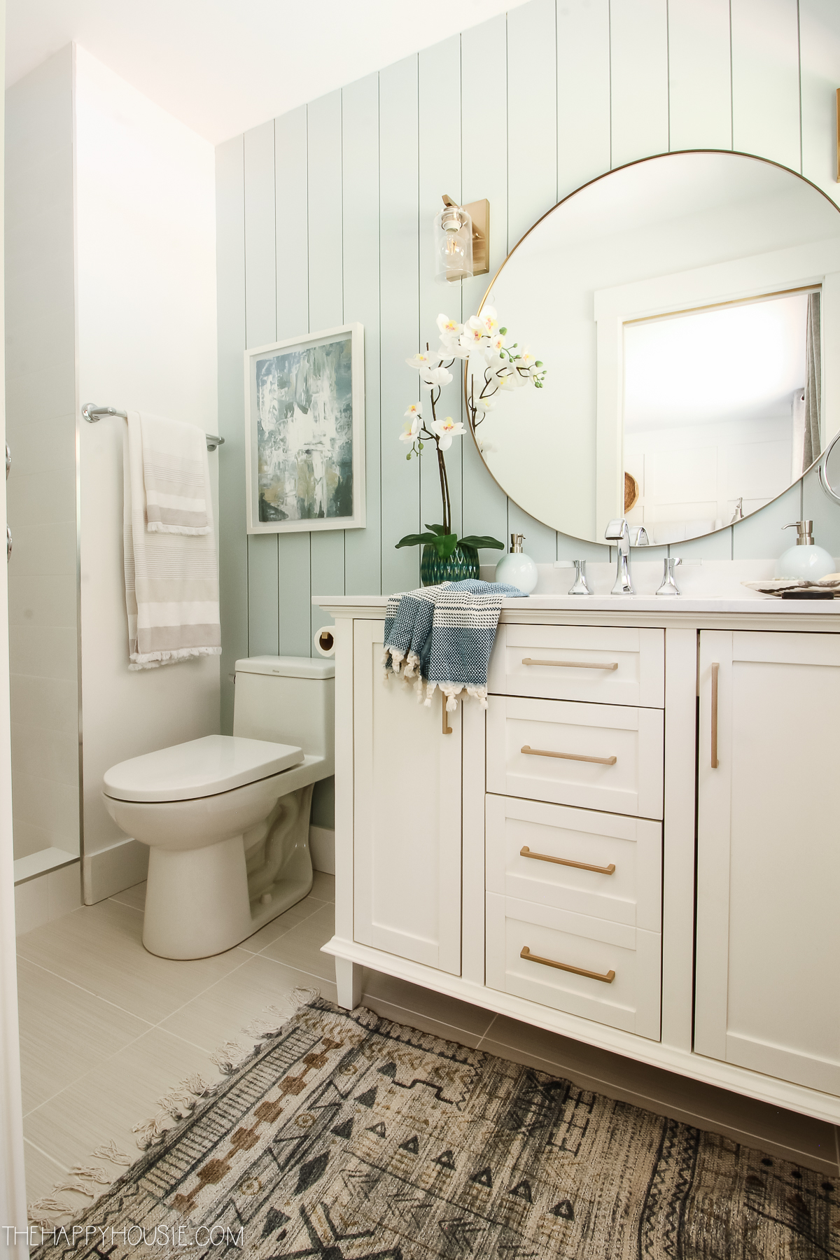 White cabinets are in the bathroom with an aqua shiplap wall.