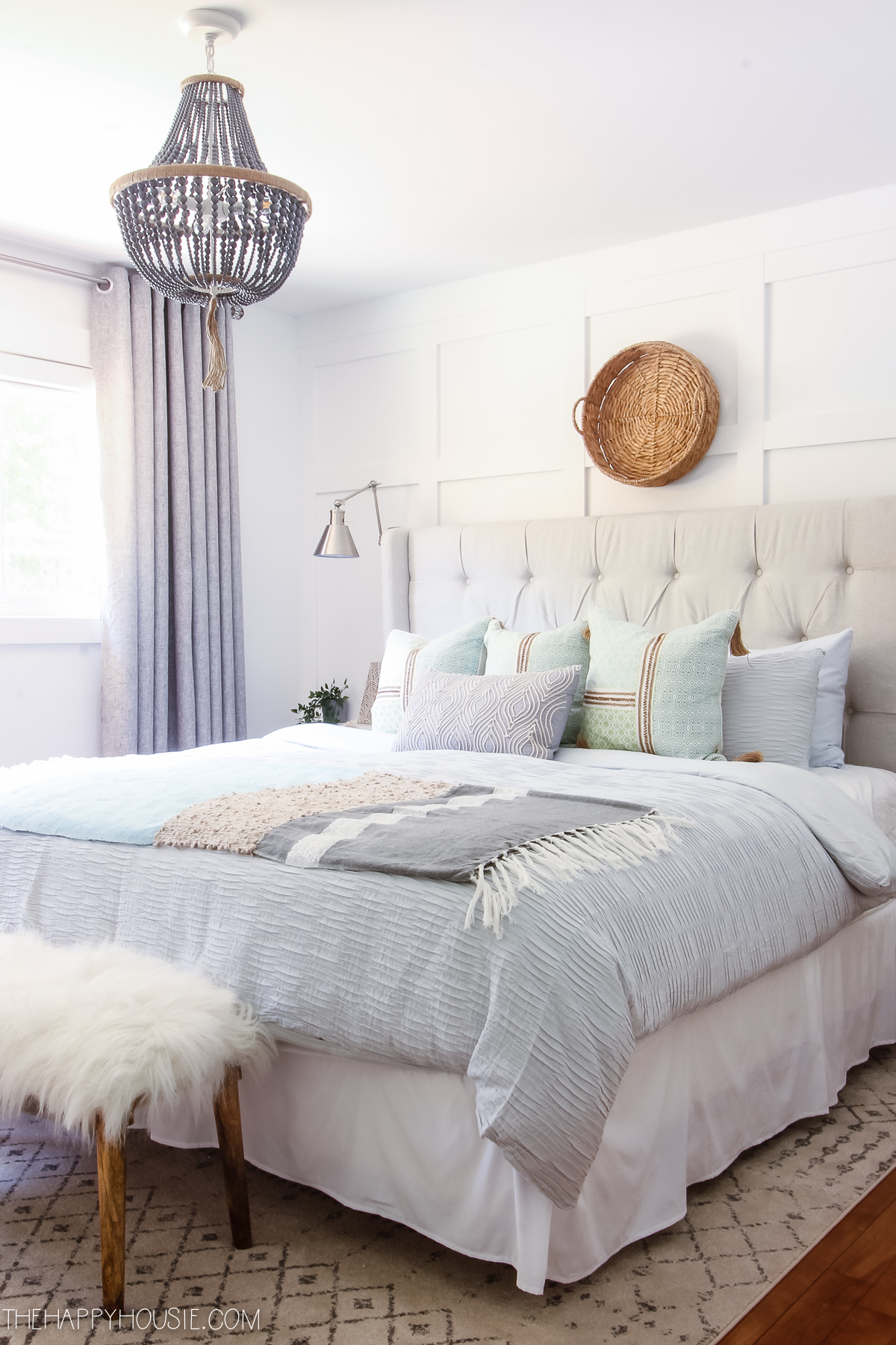 A bright bedroom with a tufted bed and a beaded chandelier above it.
