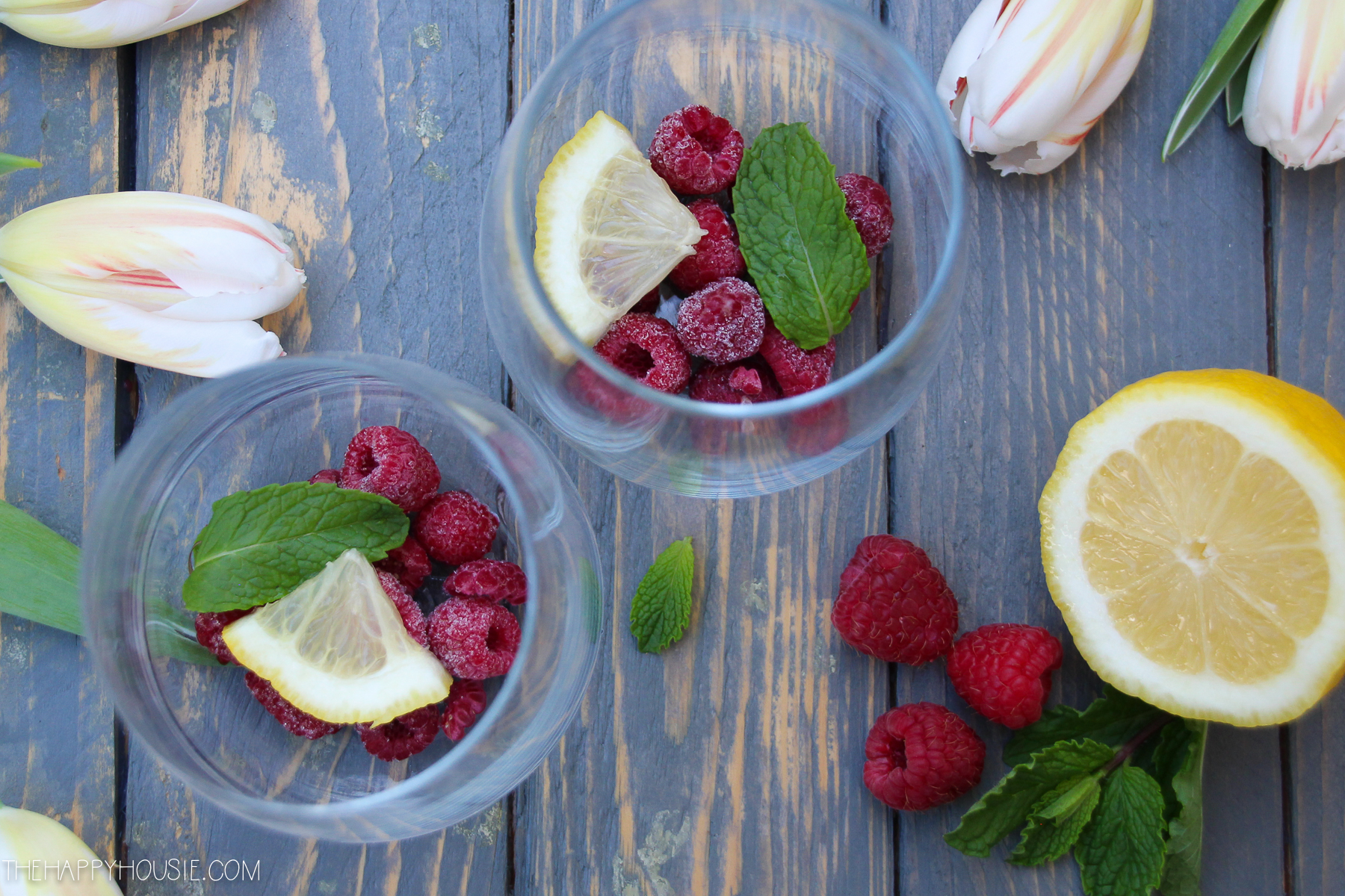 Raspberries, a cut lemon, and mint in the bottom of a glass.