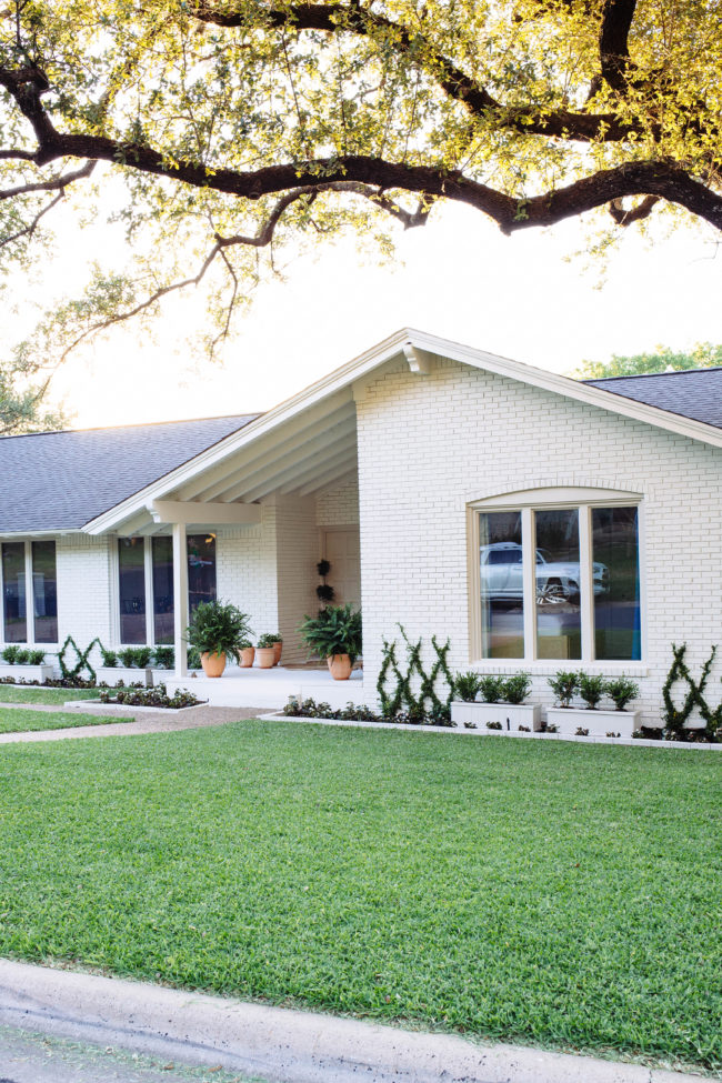 This white brick home has greenery out front and a large green lawn.