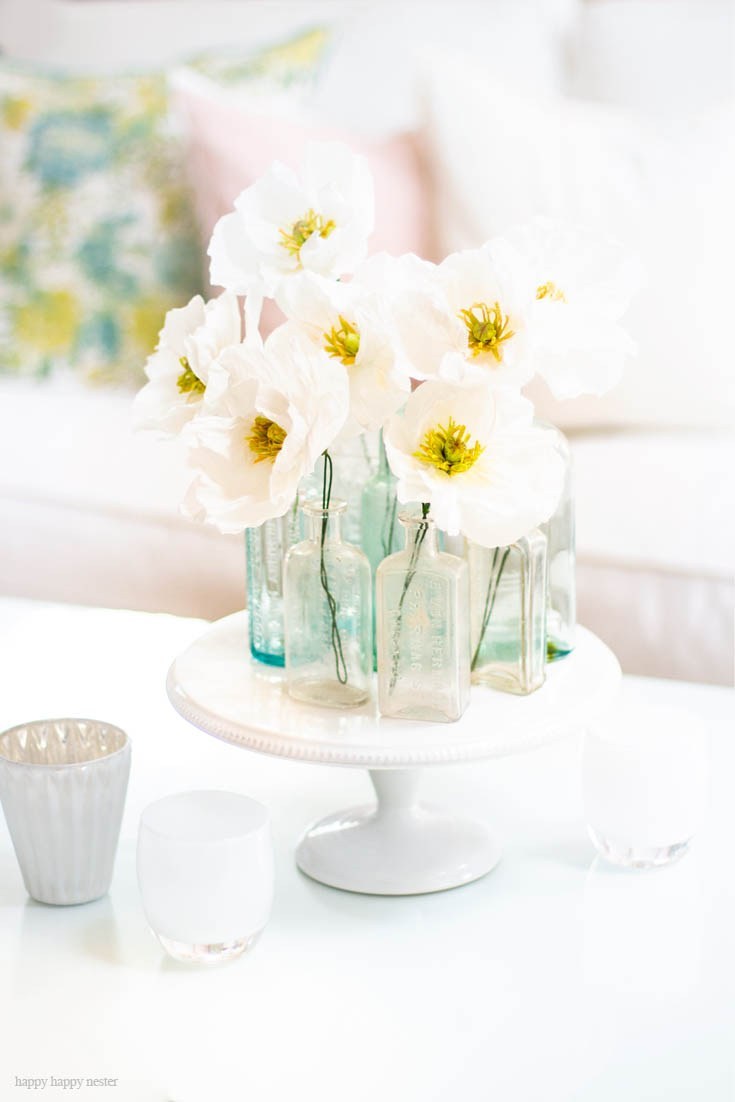 White flowers with a yellow inside in clear vases on a cake stand.