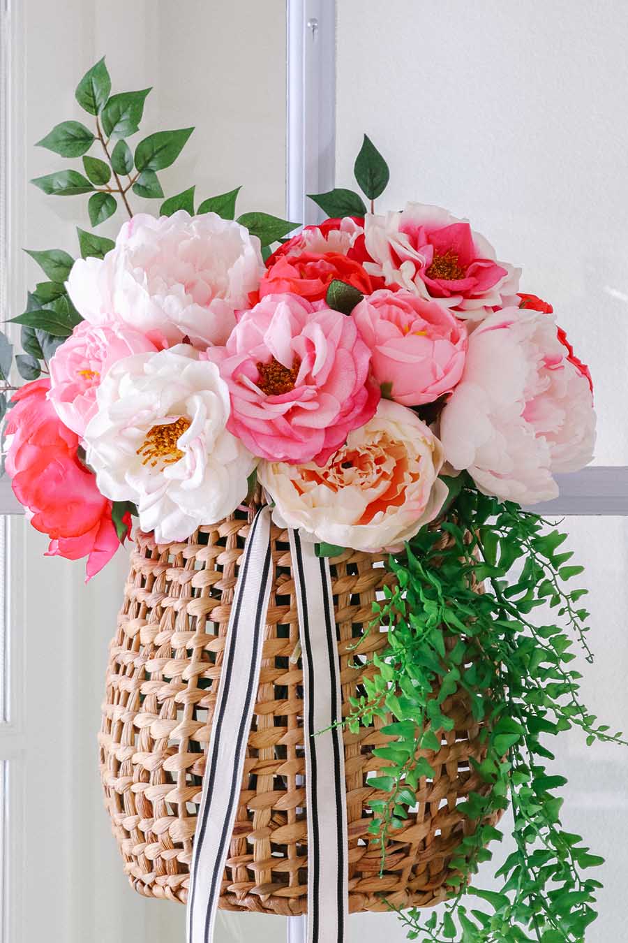 A wicker basket filled with pink and white flowers and green branches.