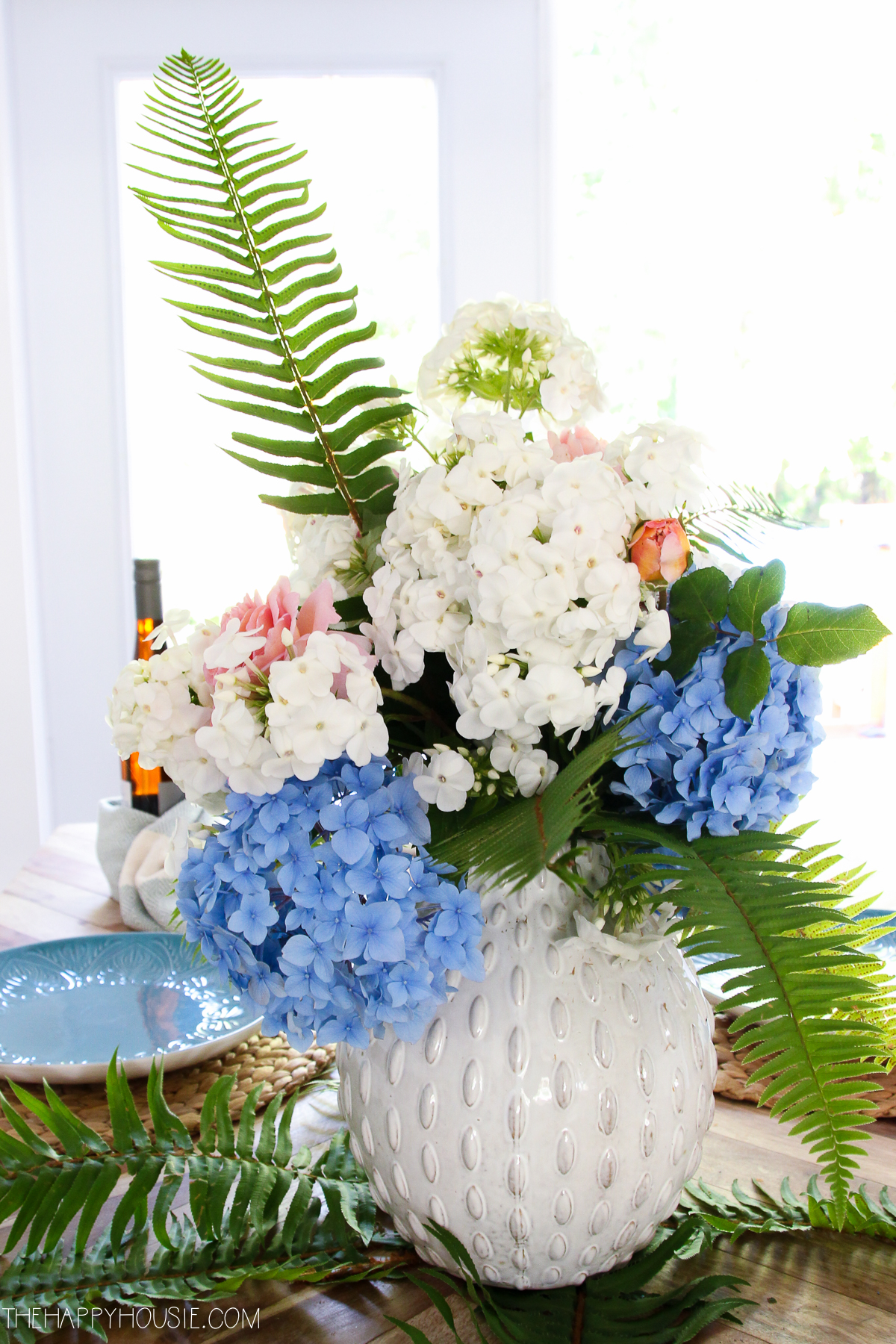 White, blue and ferns in a white vase on the table.