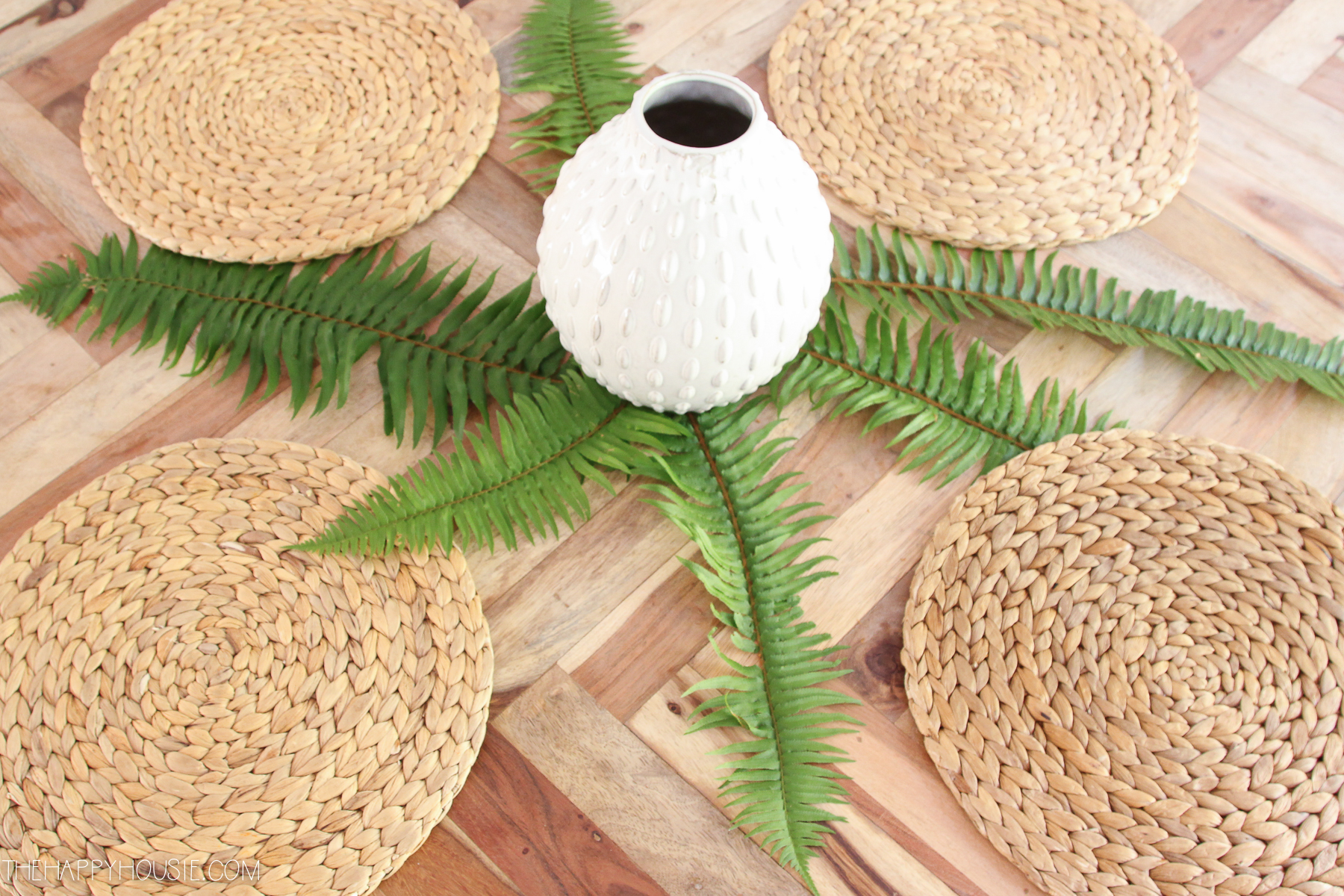 A white vase laid out with ferns underneath and sisal placemats around it.