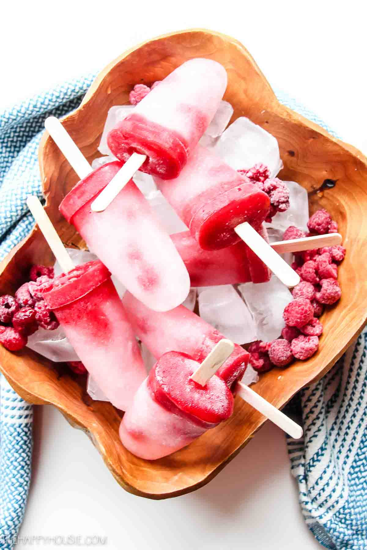 The frozen popsicles in a wooden bowl with berries around them.