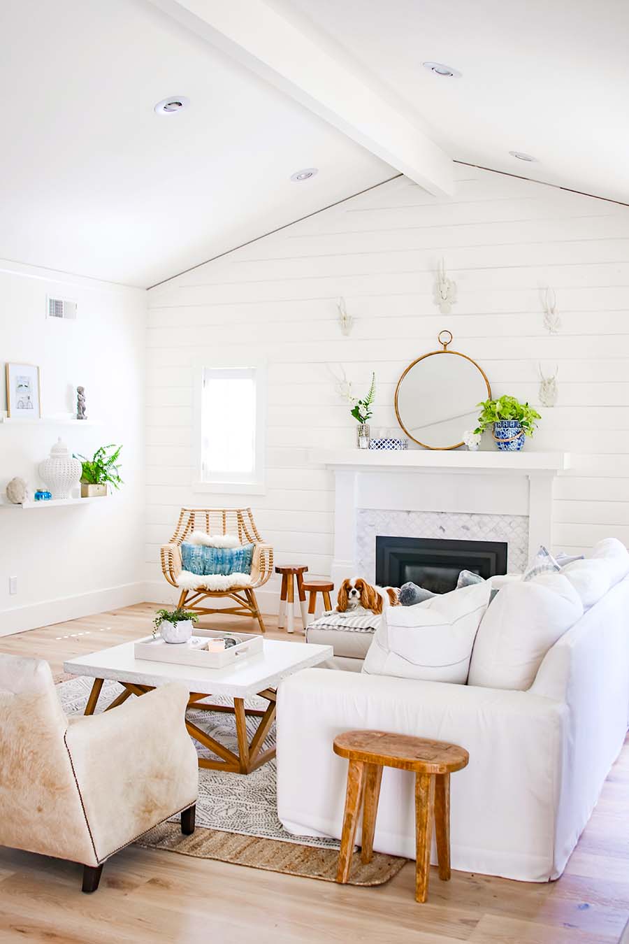 The white living room decor has pops of wood in a mirror and a step stool.