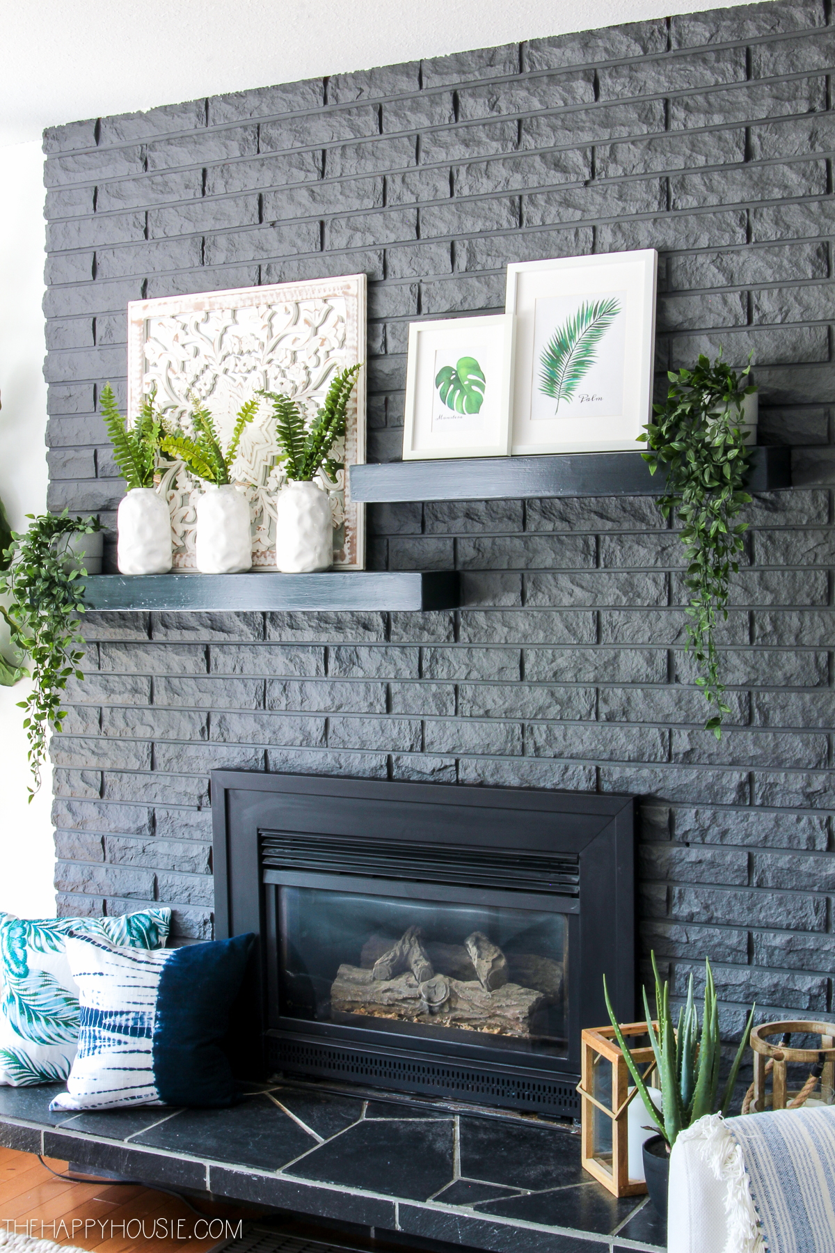 The fireplace mantel is a dark grey and has small shelves with framed prints on it.