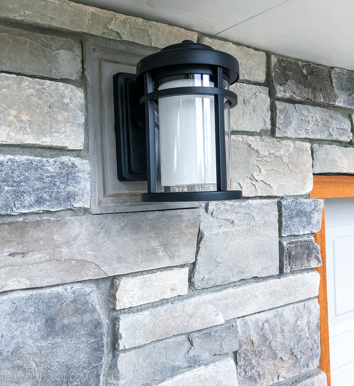 A small black light hanging on the cultured stone of the house.