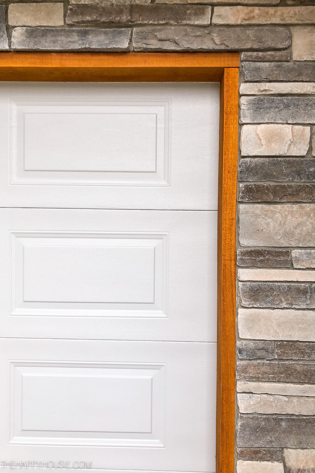 A white garage door, cedar trim and stone work.