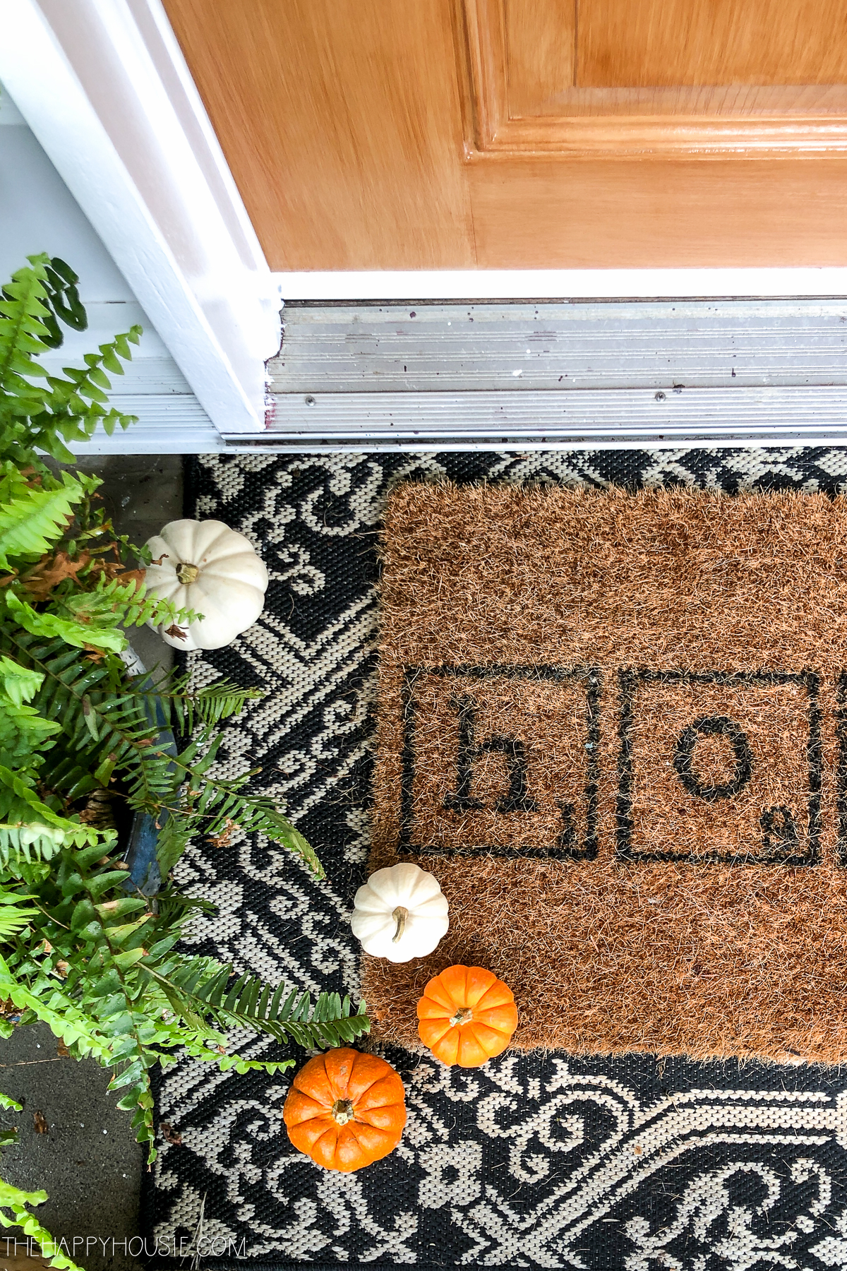 A front door mat with mini pumpkins on it.