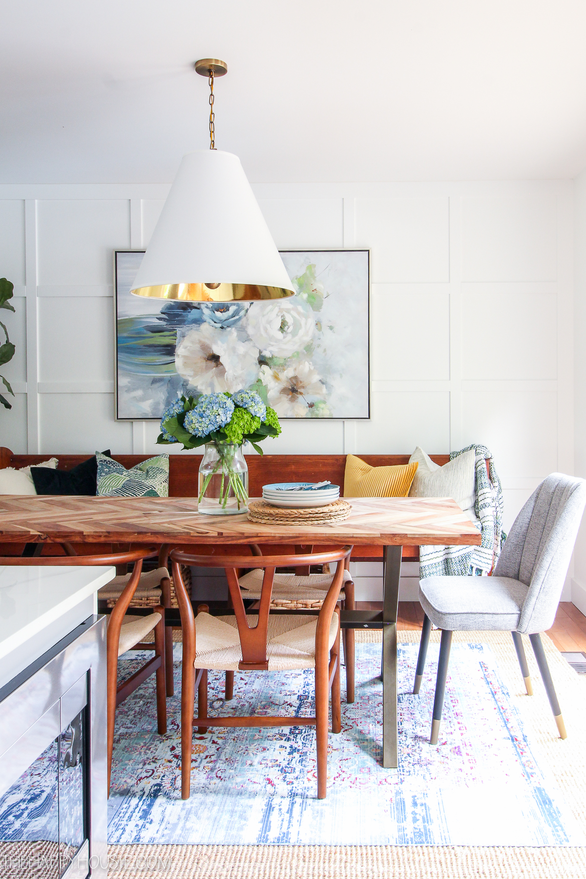A wooden dining room table with a white and brass light above it.