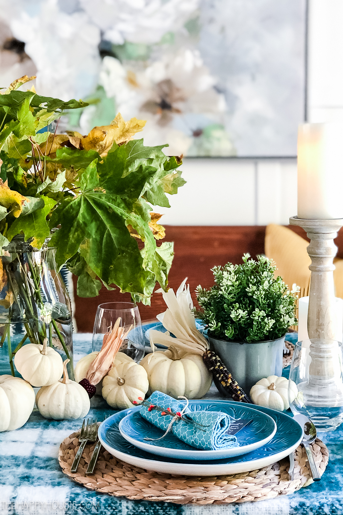 A table setting with blue plates and white mini pumpkins as the centerpiece.
