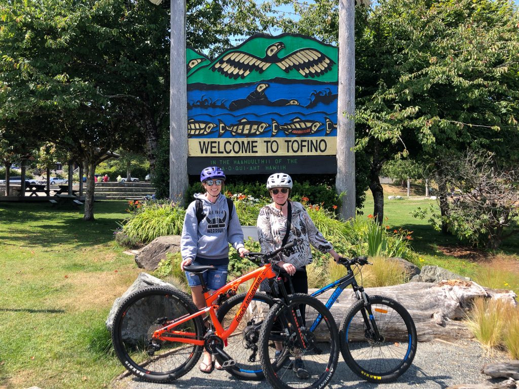 The boys on bikes in front of a welcome sign to Tofino.
