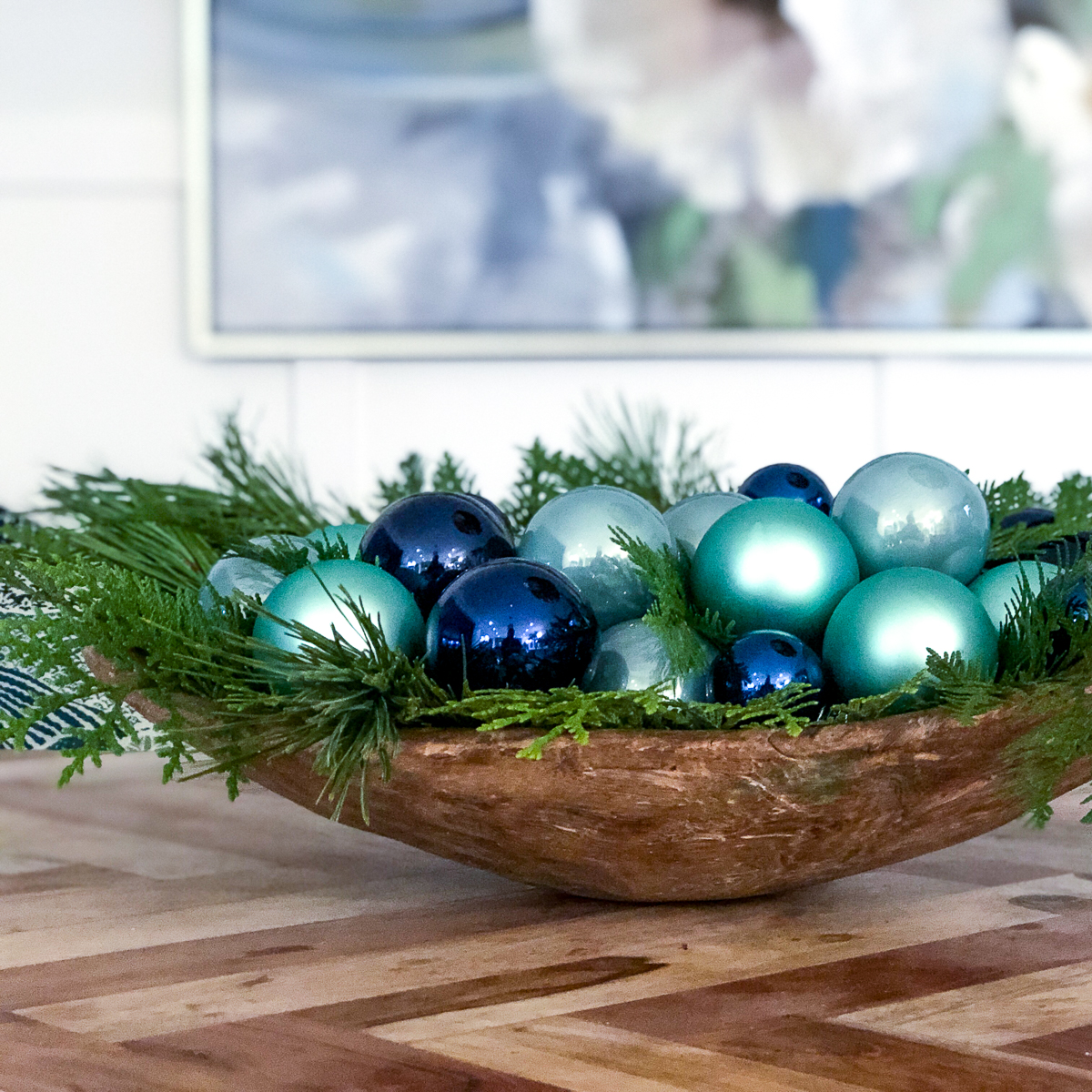 A wooden bowl with the evergreen branches and ornaments in it.
