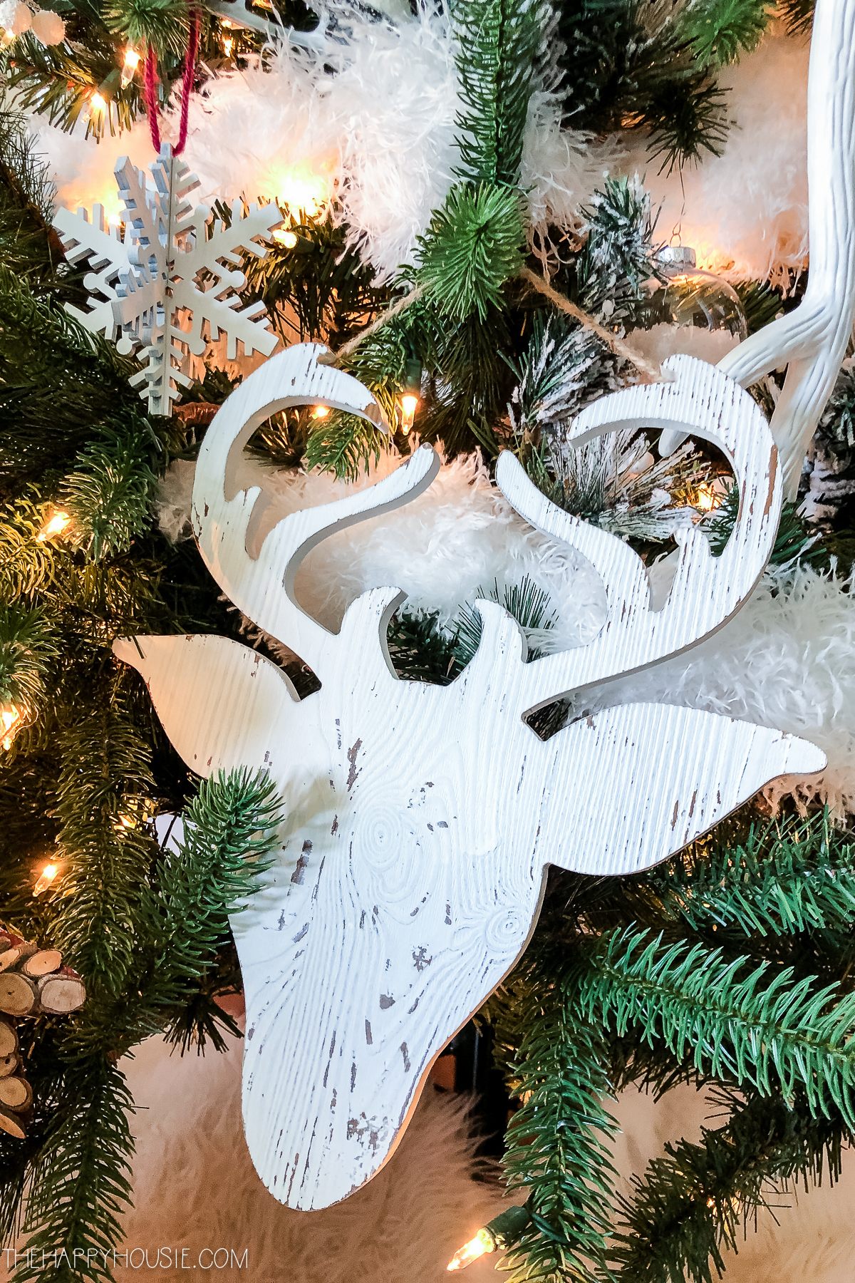 A wooden deer with antlers is sitting on the Christmas tree.