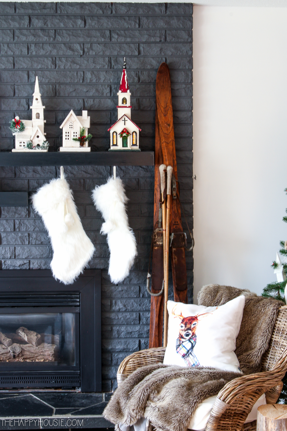There is a white pillow with a deer on it on the chair beside the fireplace.