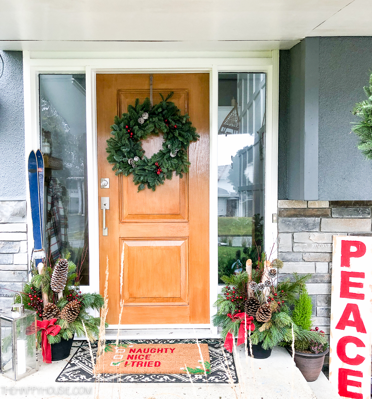 A front door with a Christmas wreath on it and holiday decorations around it.