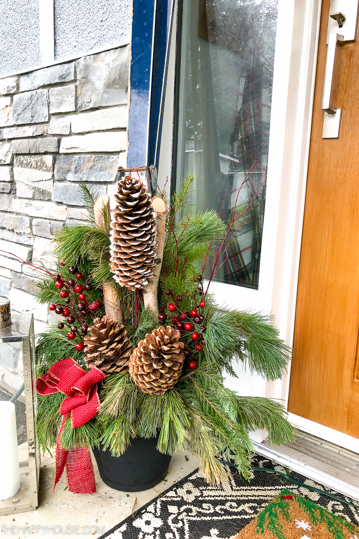 A planter filled with pine cones and greenery with a red ribbon.