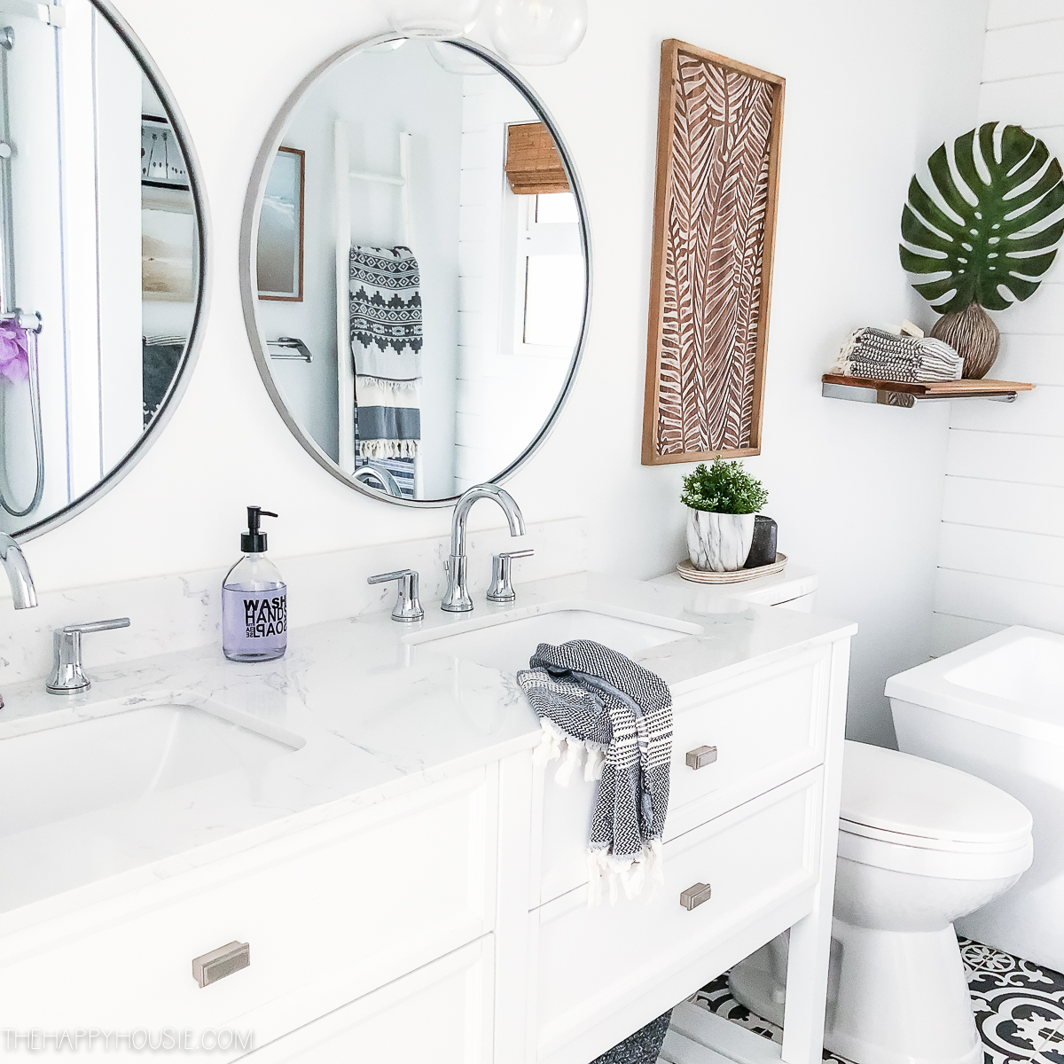 A white bathroom with round mirrors and a pam leaf in the corner.