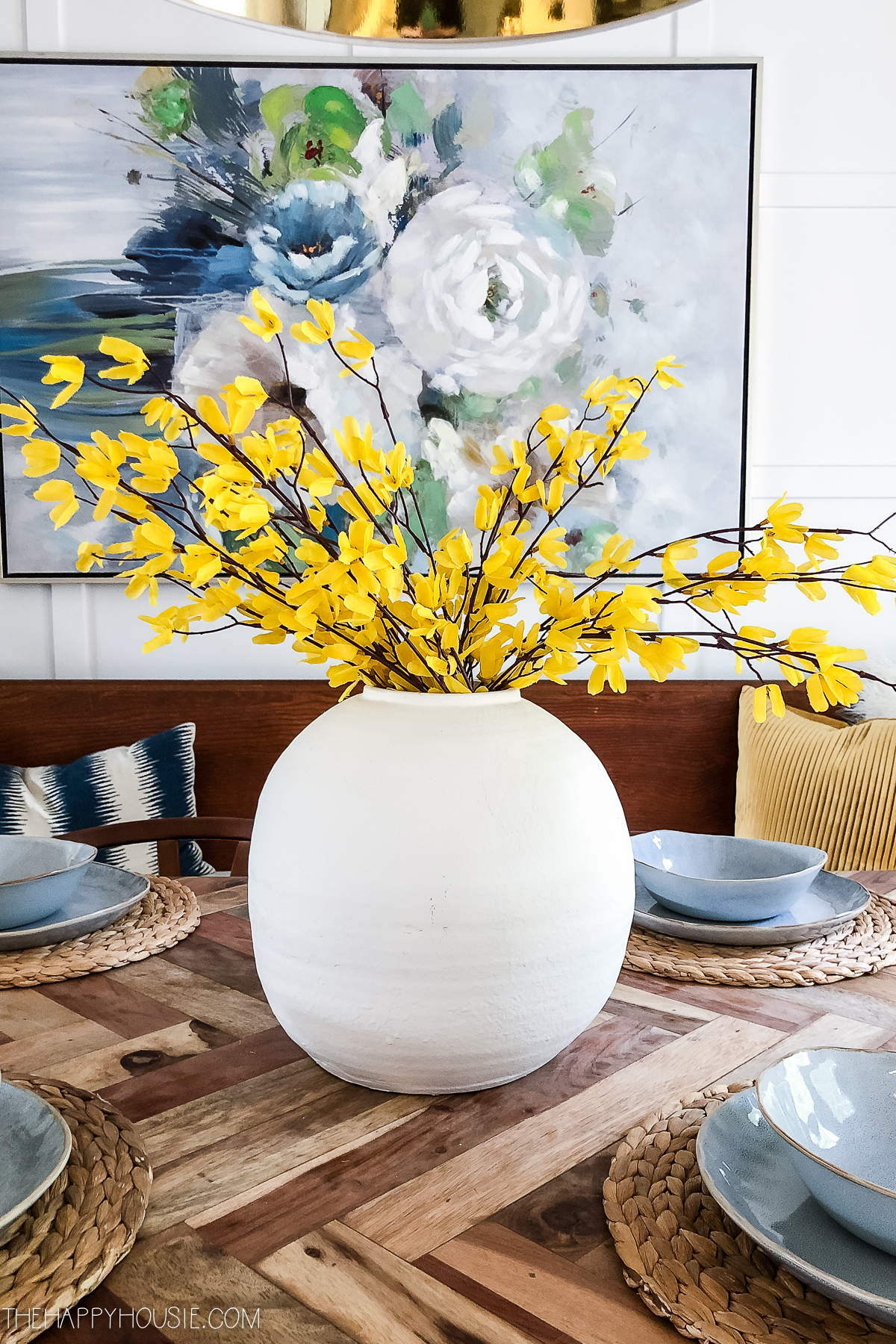 The bold yellow blooms in the white vase as a centerpiece on the table.