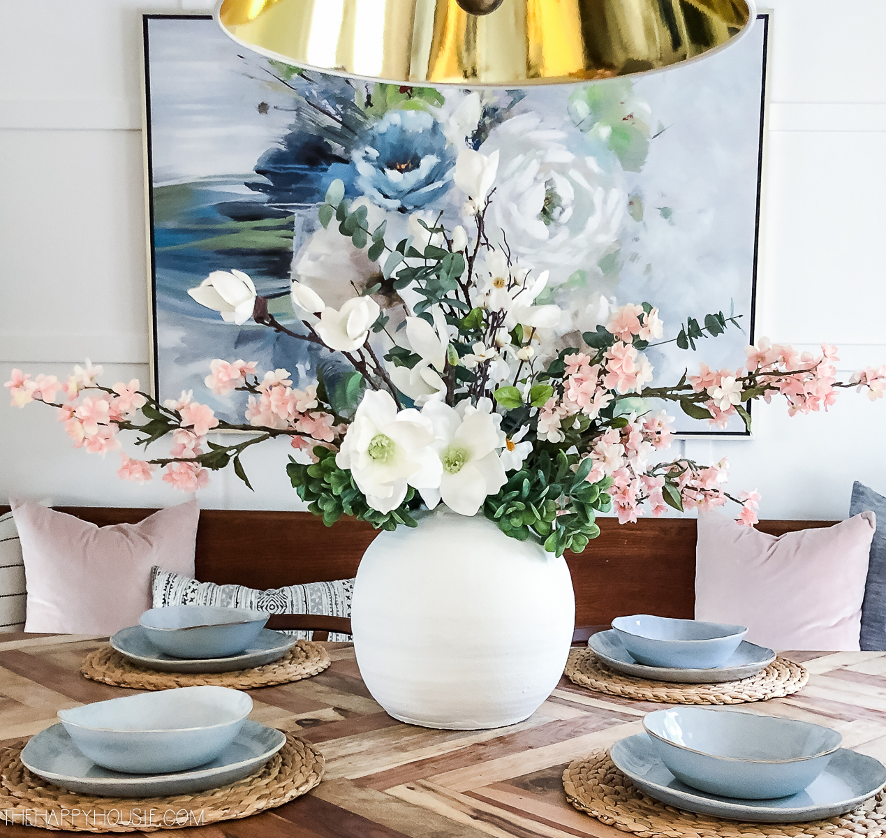 There is a white vase on the dining room table with white and pink flowers.