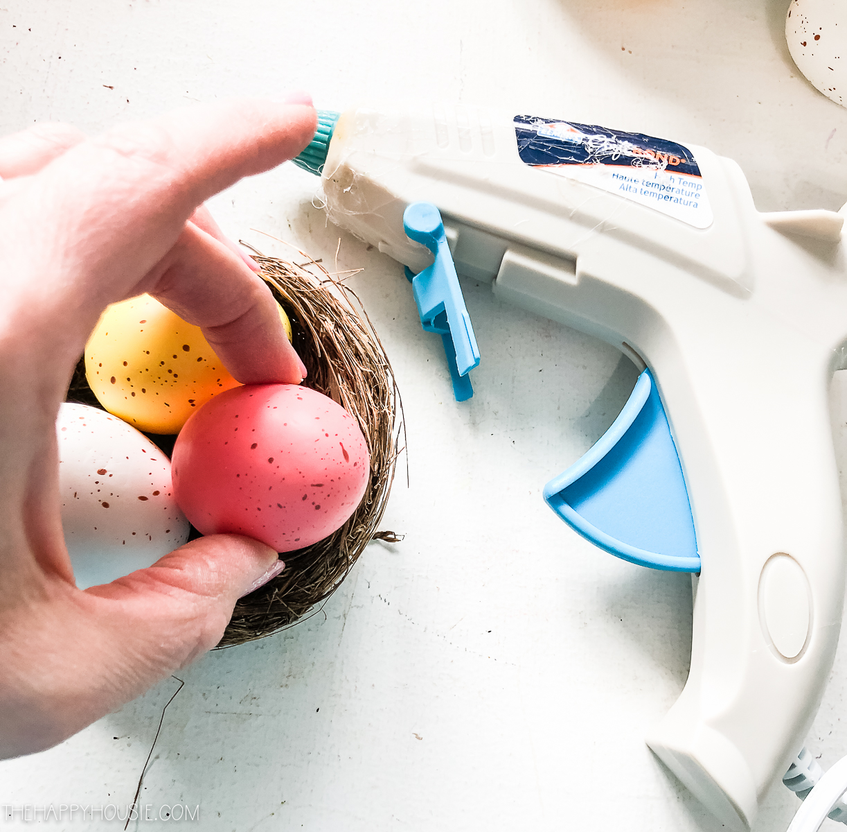 Holding a faux Easter egg beside a hot glue gun.