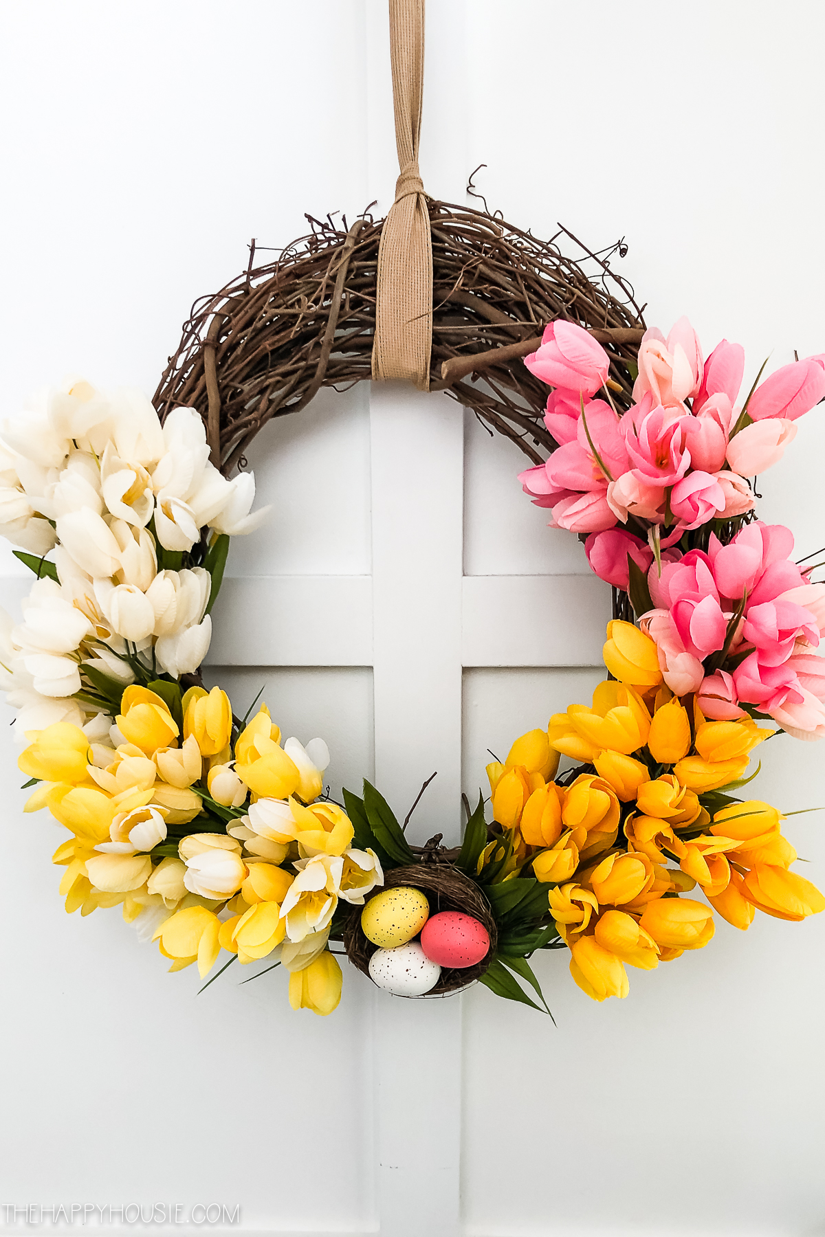 A spring wreath with pink, yellow, and white faux tulips on it.