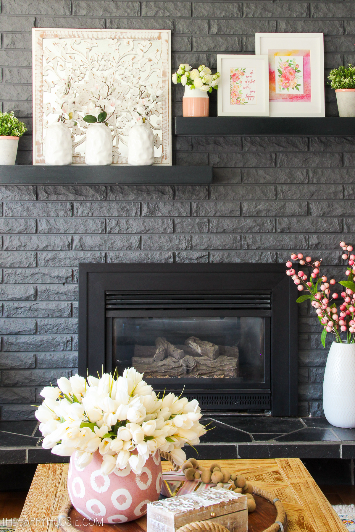 Black shelves with pictures and vases are above the fireplace.