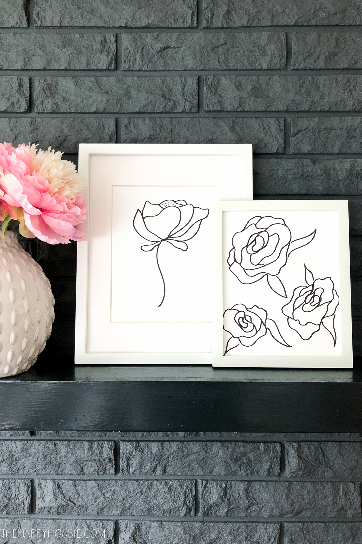 A white vase with a pink and white peony sitting beside the drawings.