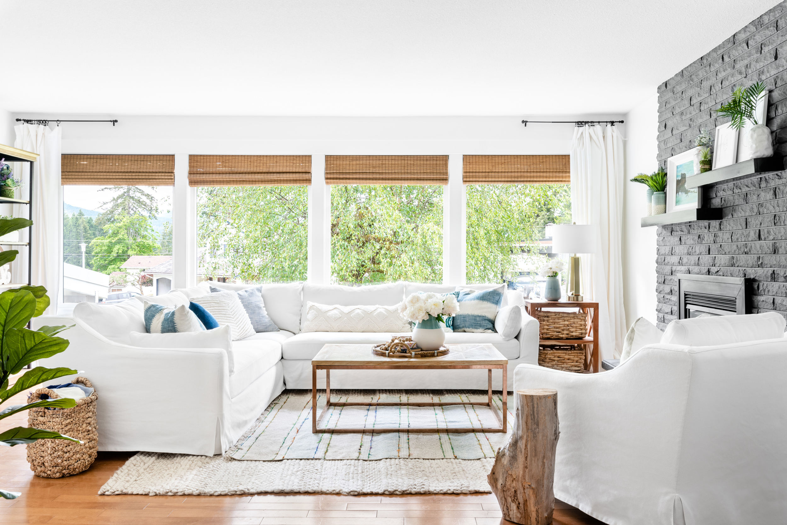 Light bright and airy living room with a white slipcovered sectional sofa and large windows with woven blinds