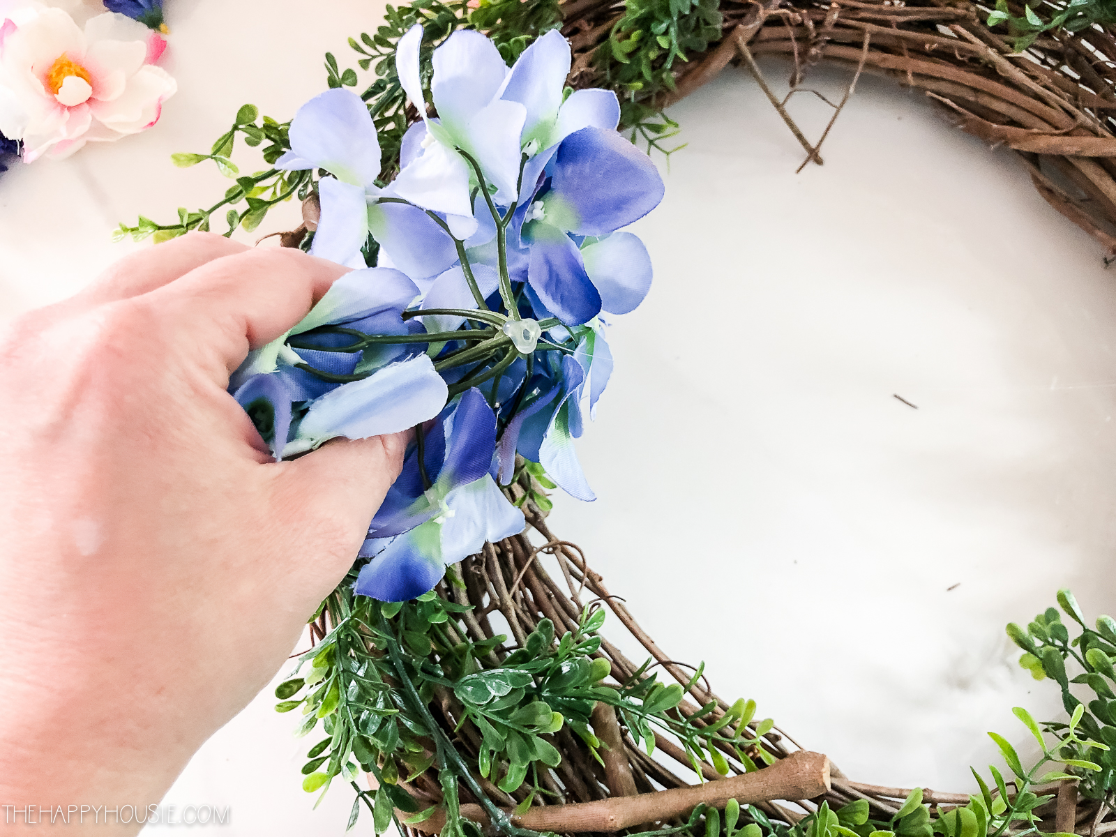 A hand placing a blue faux flower on the wreath.