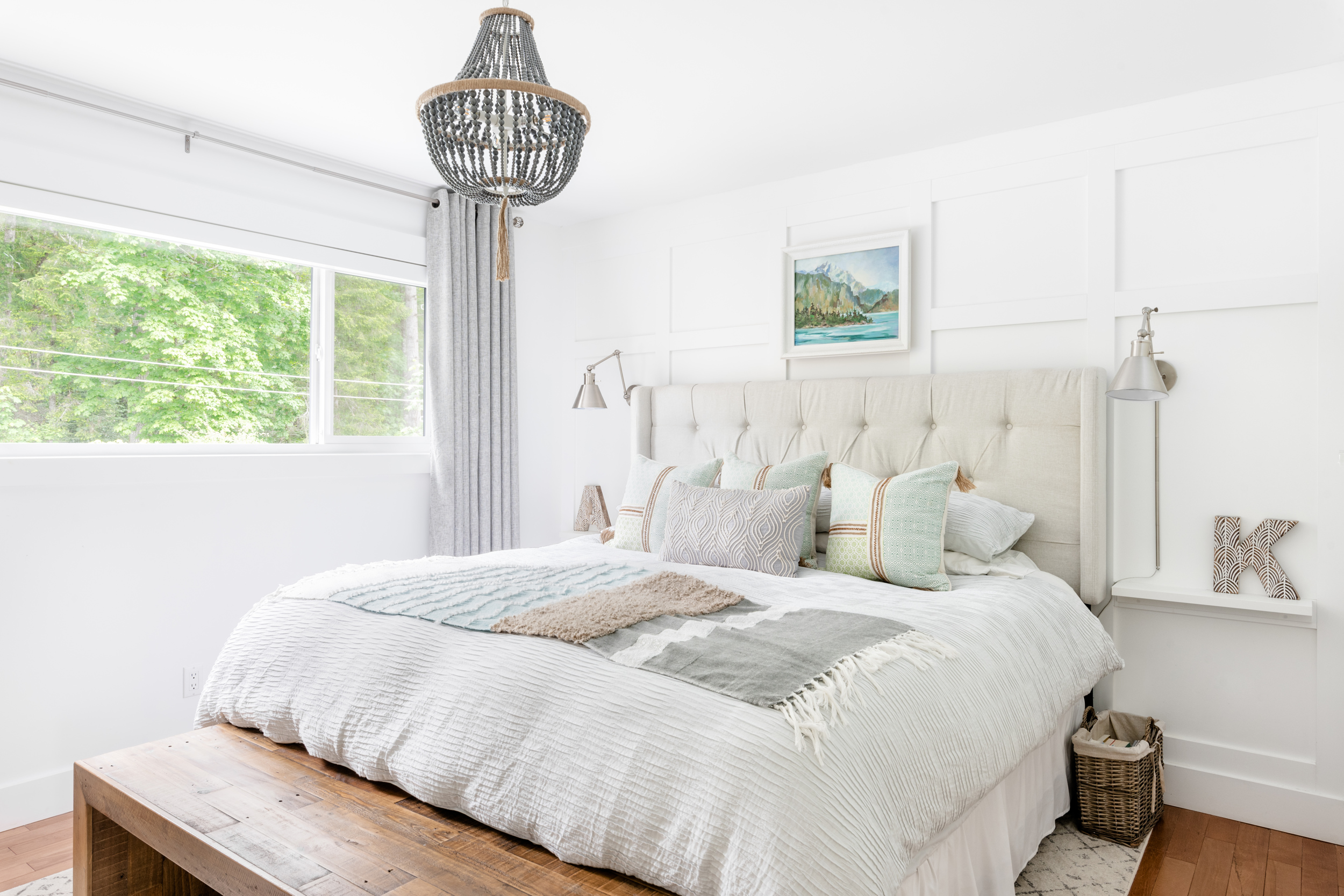 a light bright newly renovated master bedroom with a tufted upholstered bed and box panel moulding feature wall