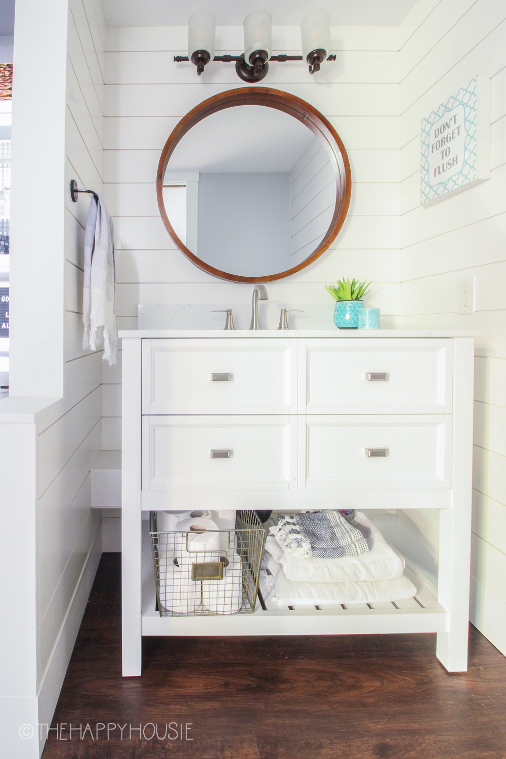A white bathroom cabinet with towels underneath and lights just above the round mirror.