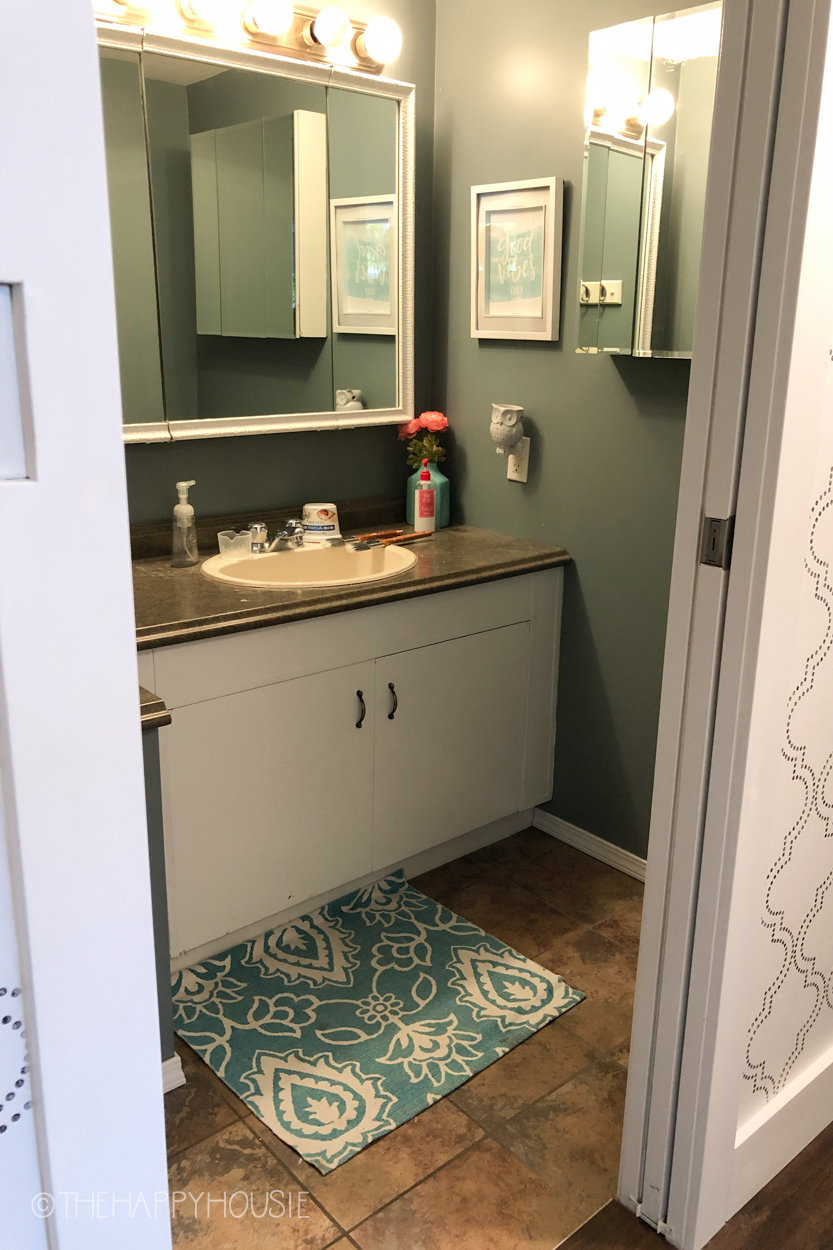The bathroom before with sage green walls, and a dated cabinet.