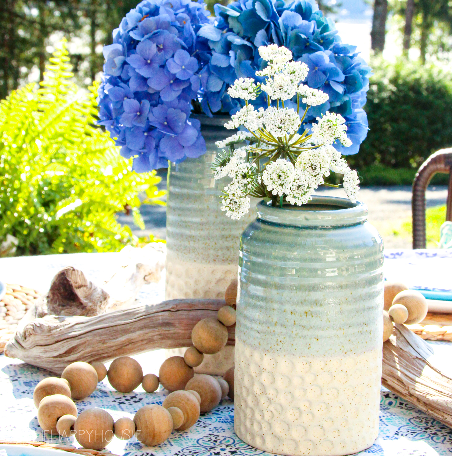 A ceramic vase with white flowers is beside the hydrangeas.